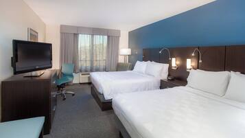 Une chambre d’hôtel avec deux lits, un bureau, une télévision, une chaise et une fenêtre avec des rideaux.