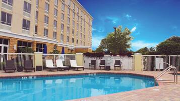 A hotel pool area with lounge chairs, a fence, and a building in the background.