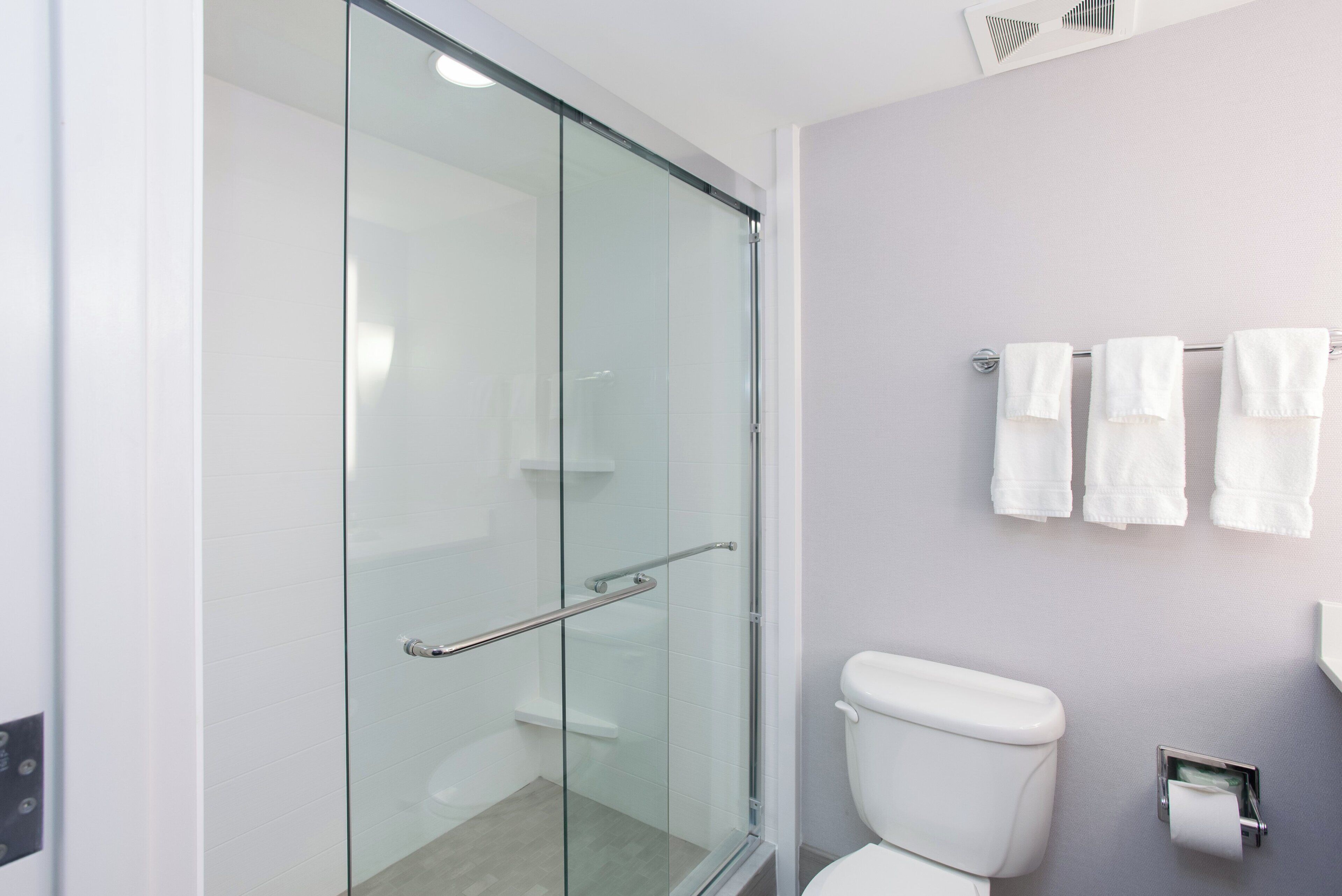 Un baño moderno con cabina de ducha de vidrio, un inodoro blanco y un perchero con varias toallas.