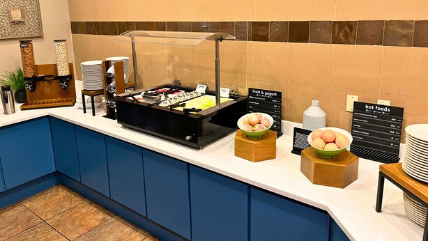 A breakfast bar with various food options, including fruit and yogurt, and a sign indicating hot foods available.