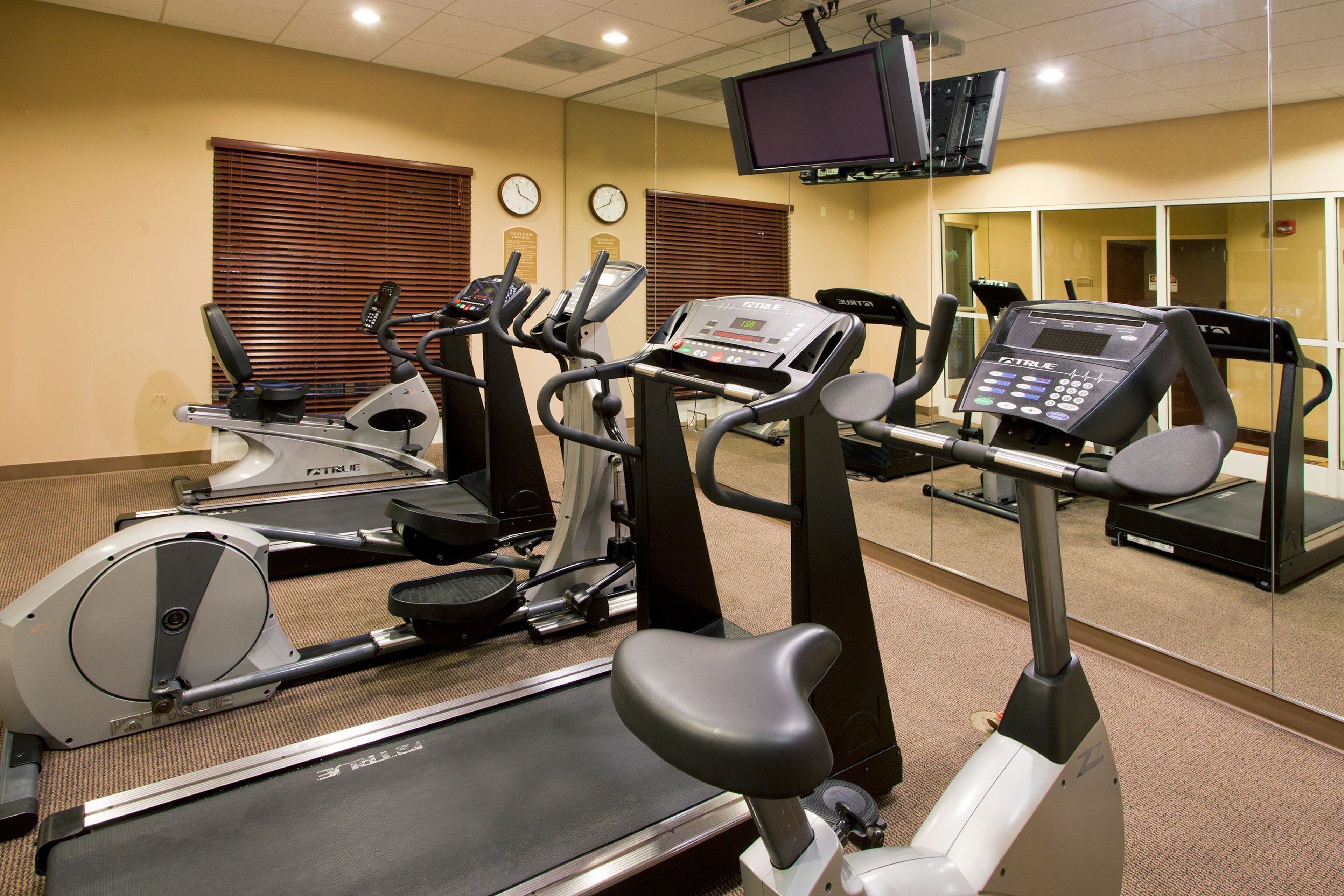 A gym with multiple cardio machines, including treadmills and ellipticals, and a television mounted on the wall.