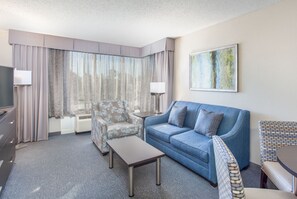 A modern hotel room with a blue sofa, a patterned armchair, a small table, and a TV on a dresser. - Holiday Inn Hotel & Suites Tallahassee Conference Ctr N by IHG (Tallahassee)