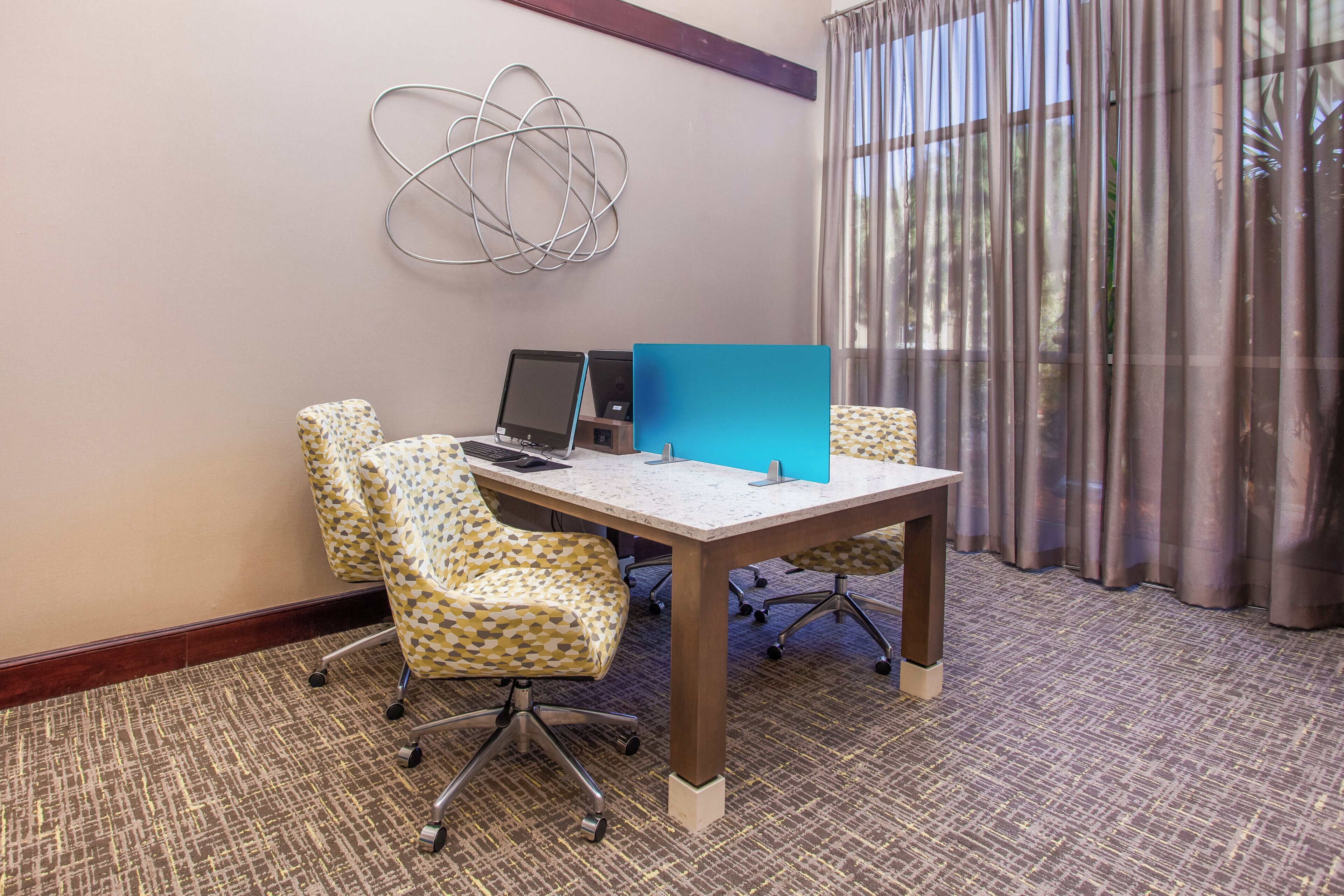 A conference room with a table, two laptops, patterned chairs, and a decorative wall piece.
