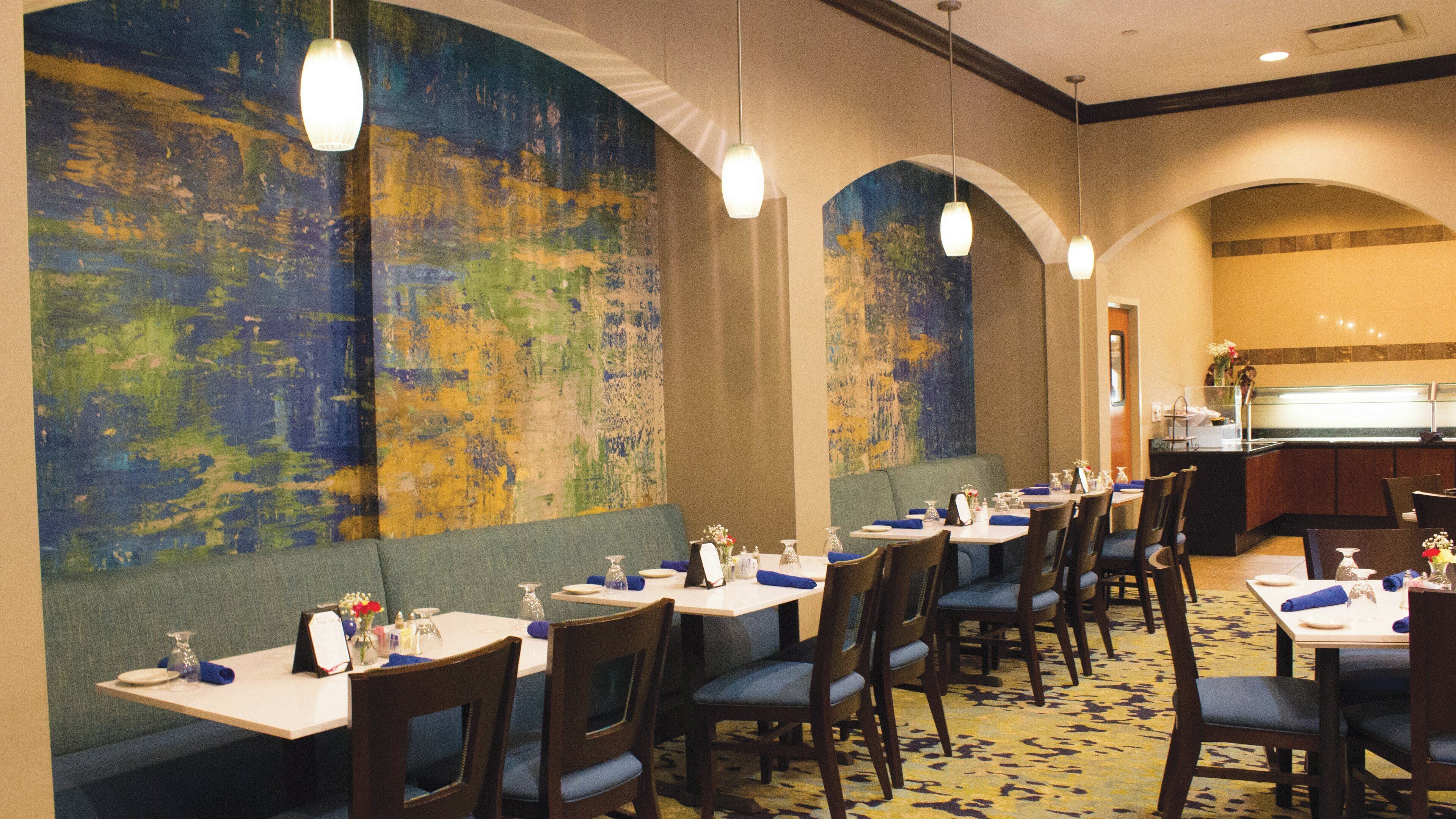 Un restaurant doté de nombreuses tables, de chaises et d’une grande fresque murale abstraite.