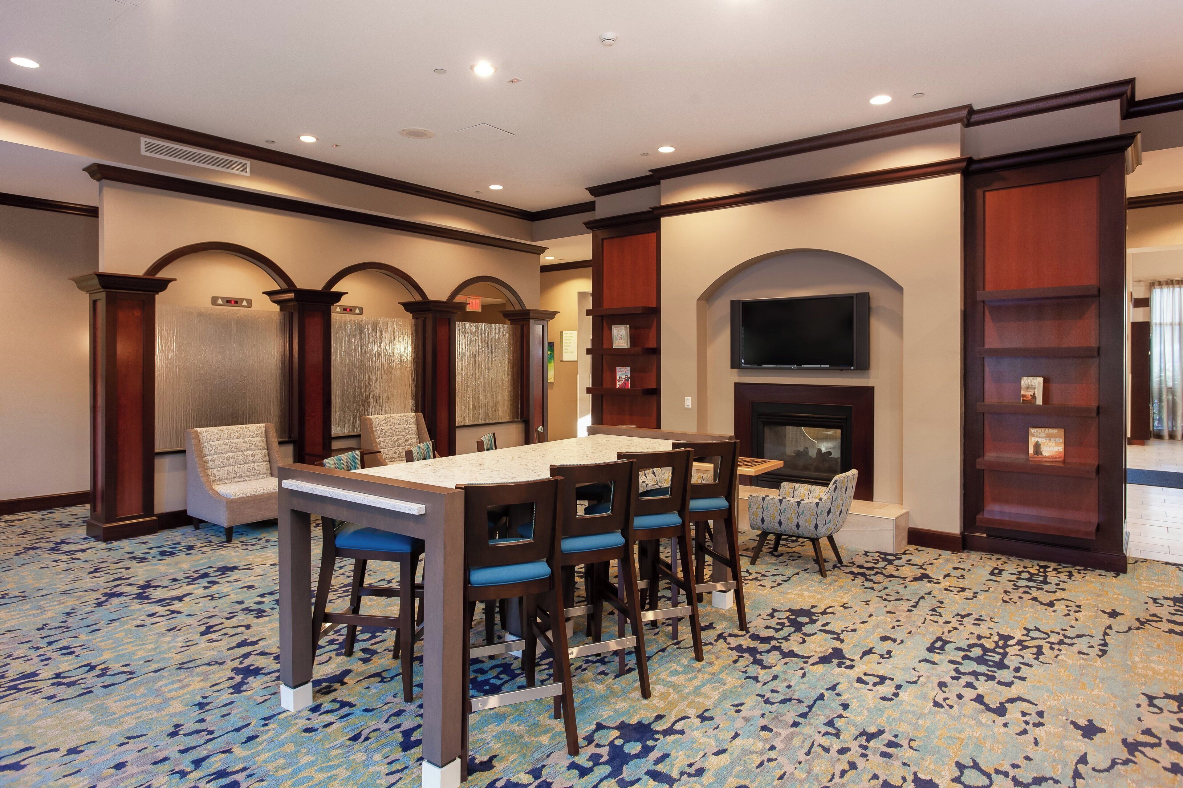 A hotel lobby with a bar area, seating, a fireplace, and a television.