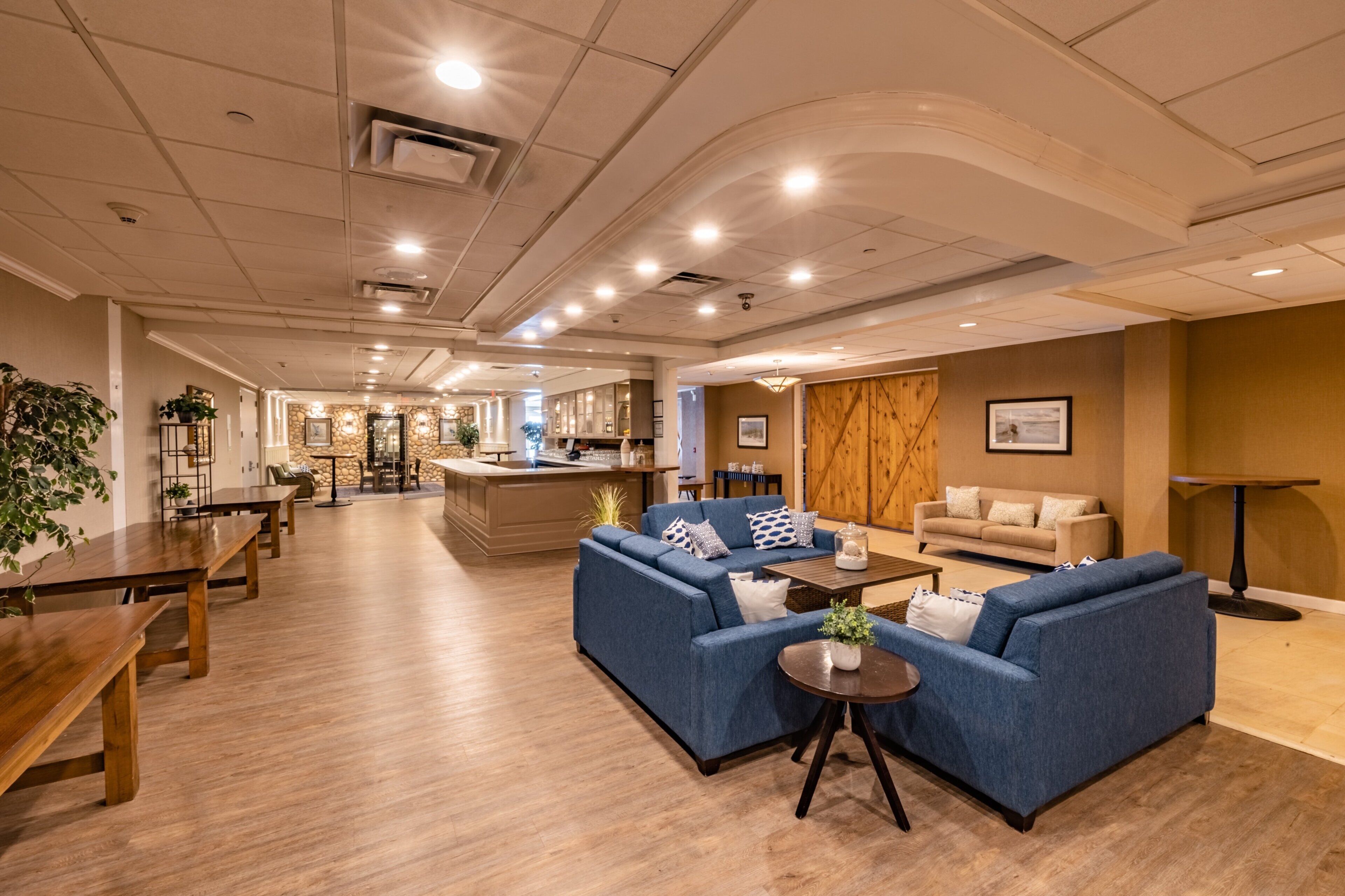 A spacious lobby with a central seating area, a kitchen in the background, and a wooden partition wall.