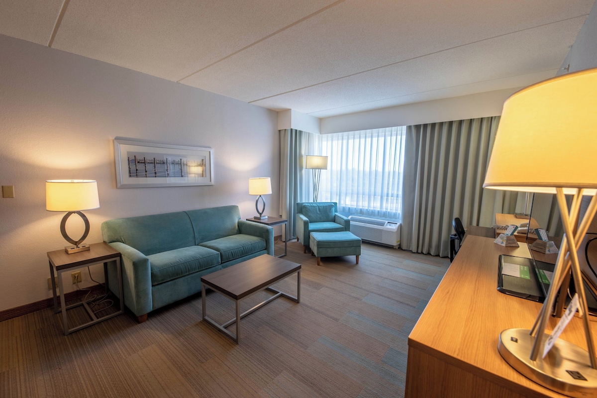 A hotel room with a sofa, a chair, a coffee table, a desk, and a lamp.