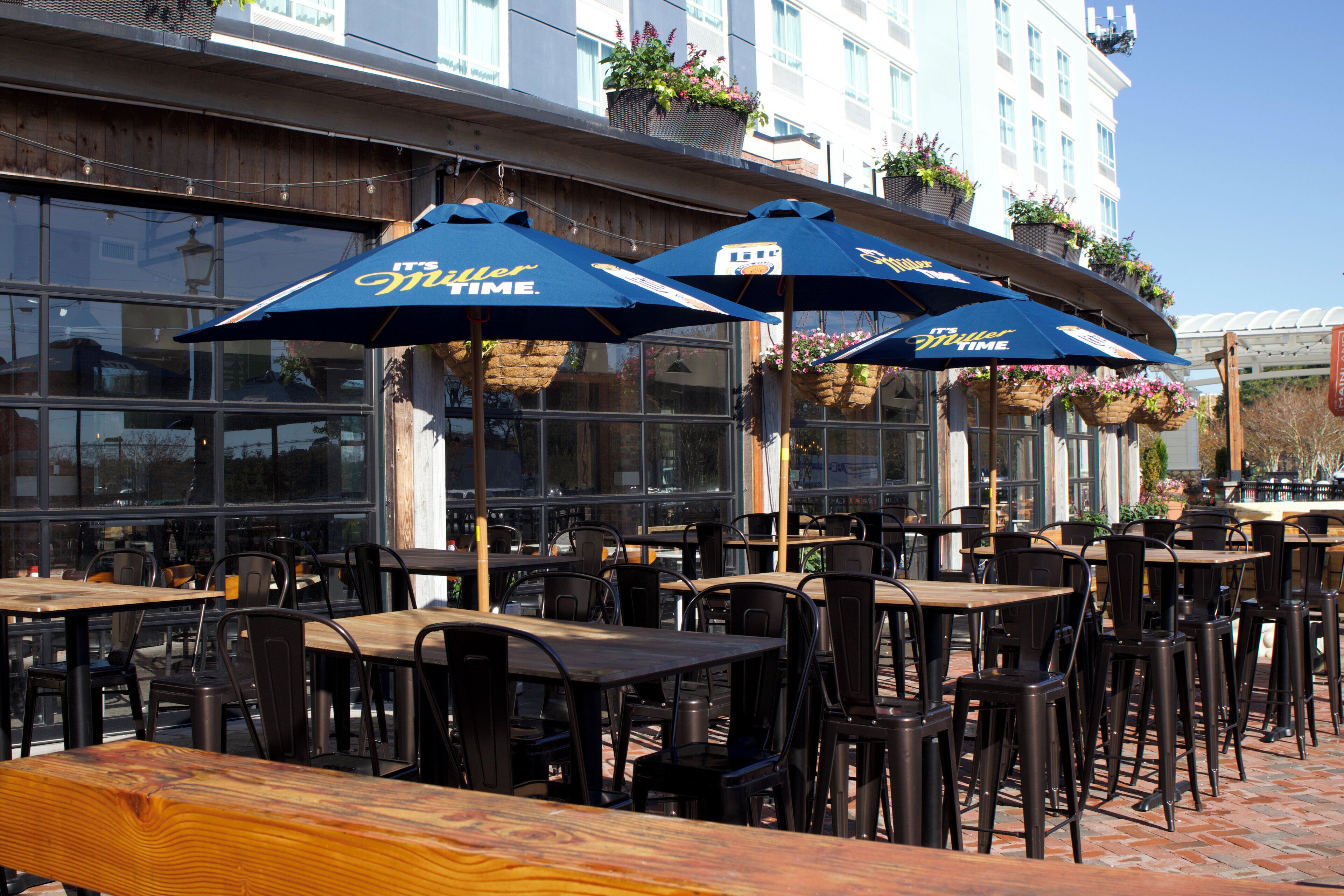 Outdoor seating with tables and chairs, blue umbrellas, and hanging flower baskets.