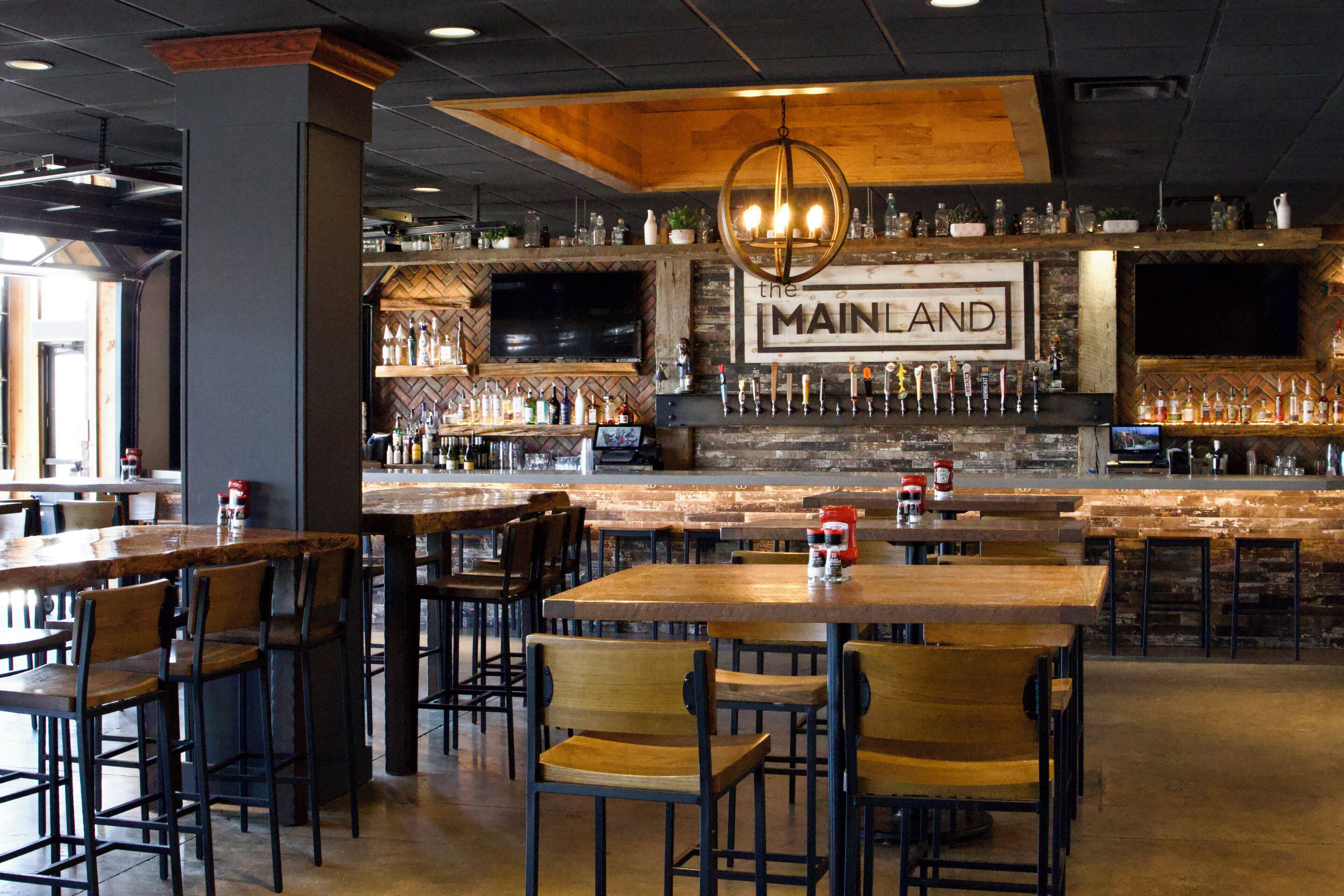 Zona de bar con diversas opciones de asientos, un televisor montado en la pared y un cartel llamativo que dice 'MAINLAND'.