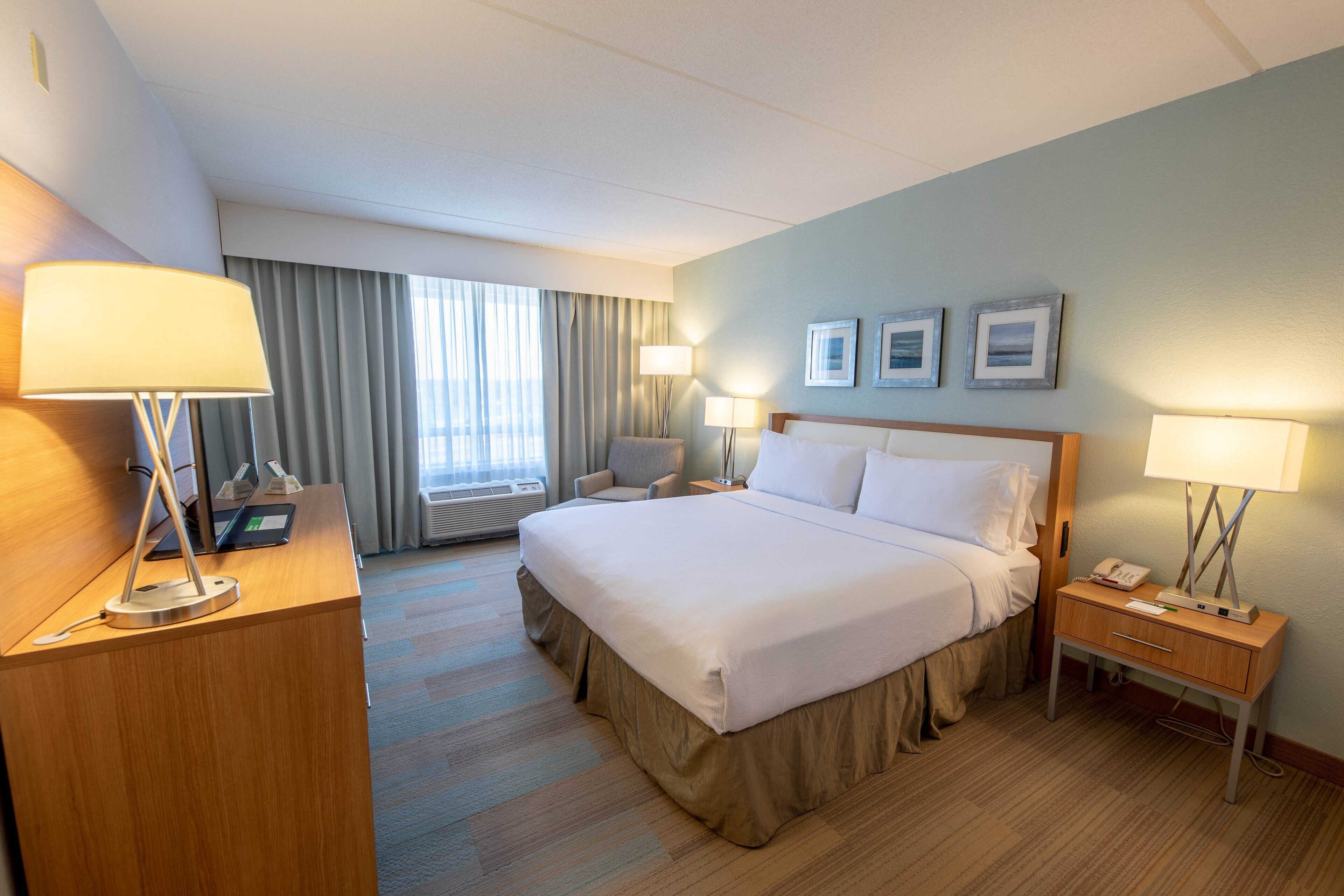 Una habitación de hotel con una cama grande, mesitas de noche, un escritorio con lámpara, una silla y una ventana con cortinas.