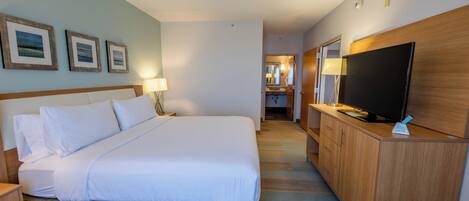 Habitación de hotel con una cama grande, un televisor sobre una cómoda de madera, un escritorio con una lámpara y cuadros en la pared.
