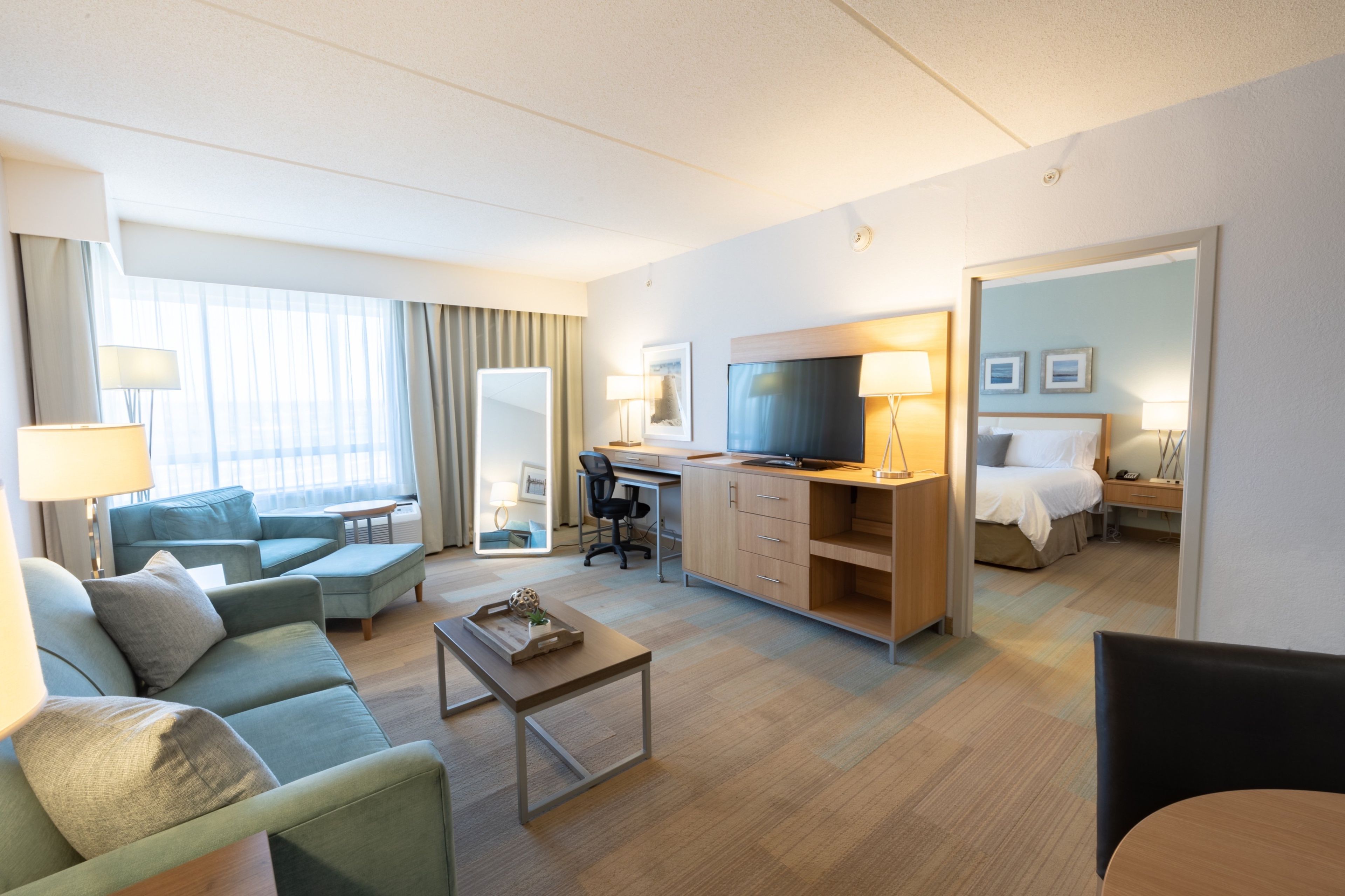 A hotel room with a sofa, a desk, a television, a bed, and a mirror.