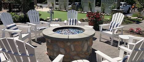 Un área de patio con sillas Adirondack blancas dispuestas alrededor de un hogar de piedra.