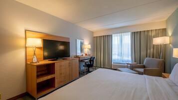 A hotel room with a large bed, a desk with a chair, a television, and a window with curtains.