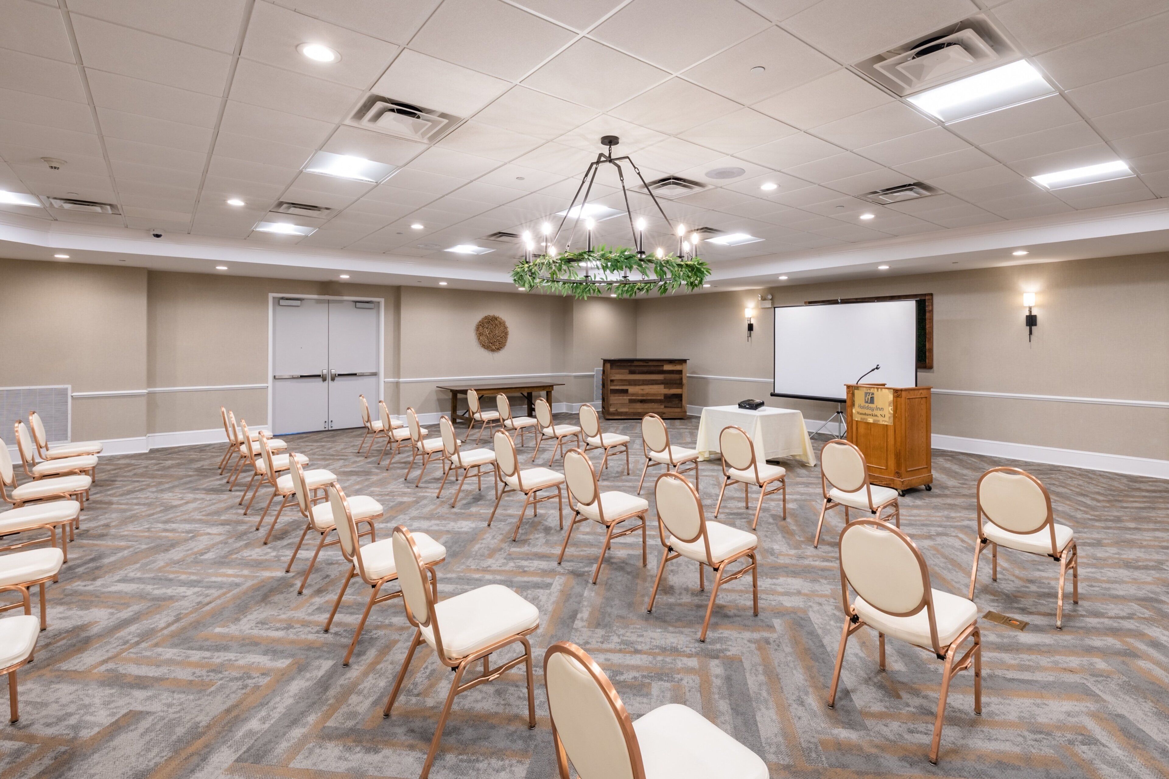 A conference room with rows of chairs, a podium, a screen, and a chandelier.