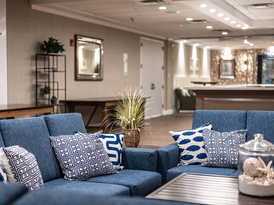 A modern lobby with a blue sofa set, patterned cushions, a potted plant, and a decorative glass jar.