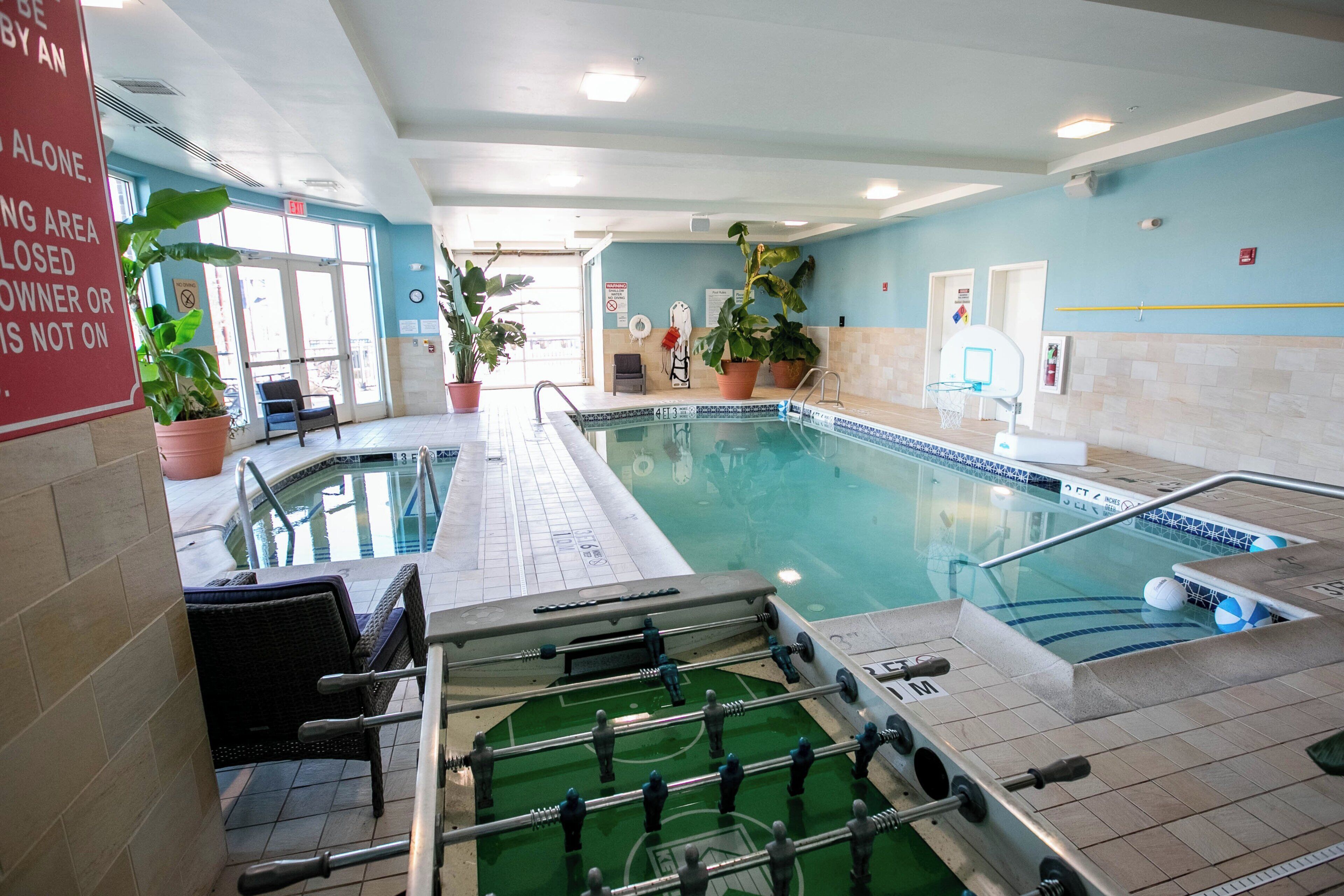 An indoor pool area with a foosball table, seating, and potted plants.