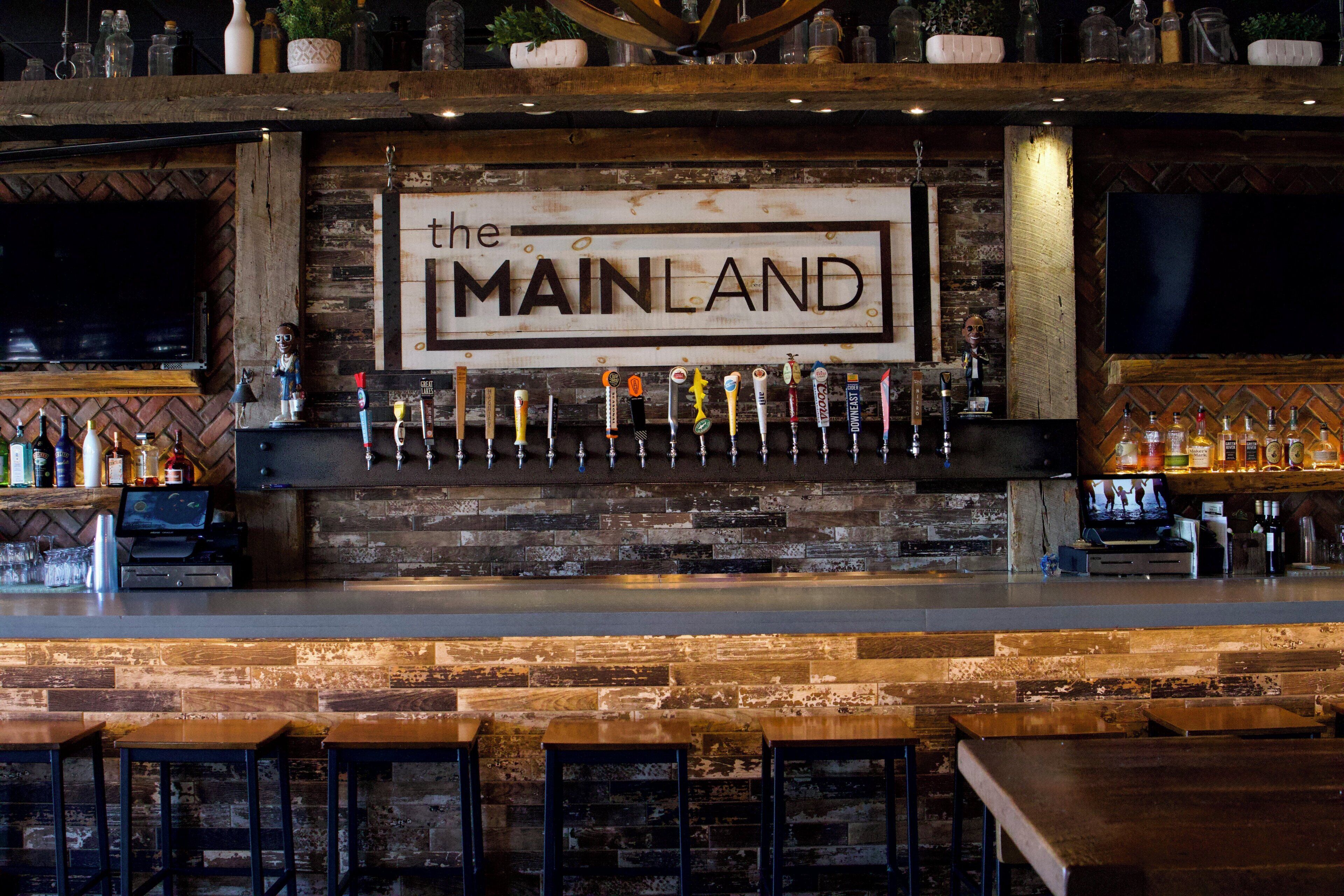 Un bar amb una paret de fusta rústica, un rètol que diu 'MAINLAND' i diverses aixetes de cervesa.