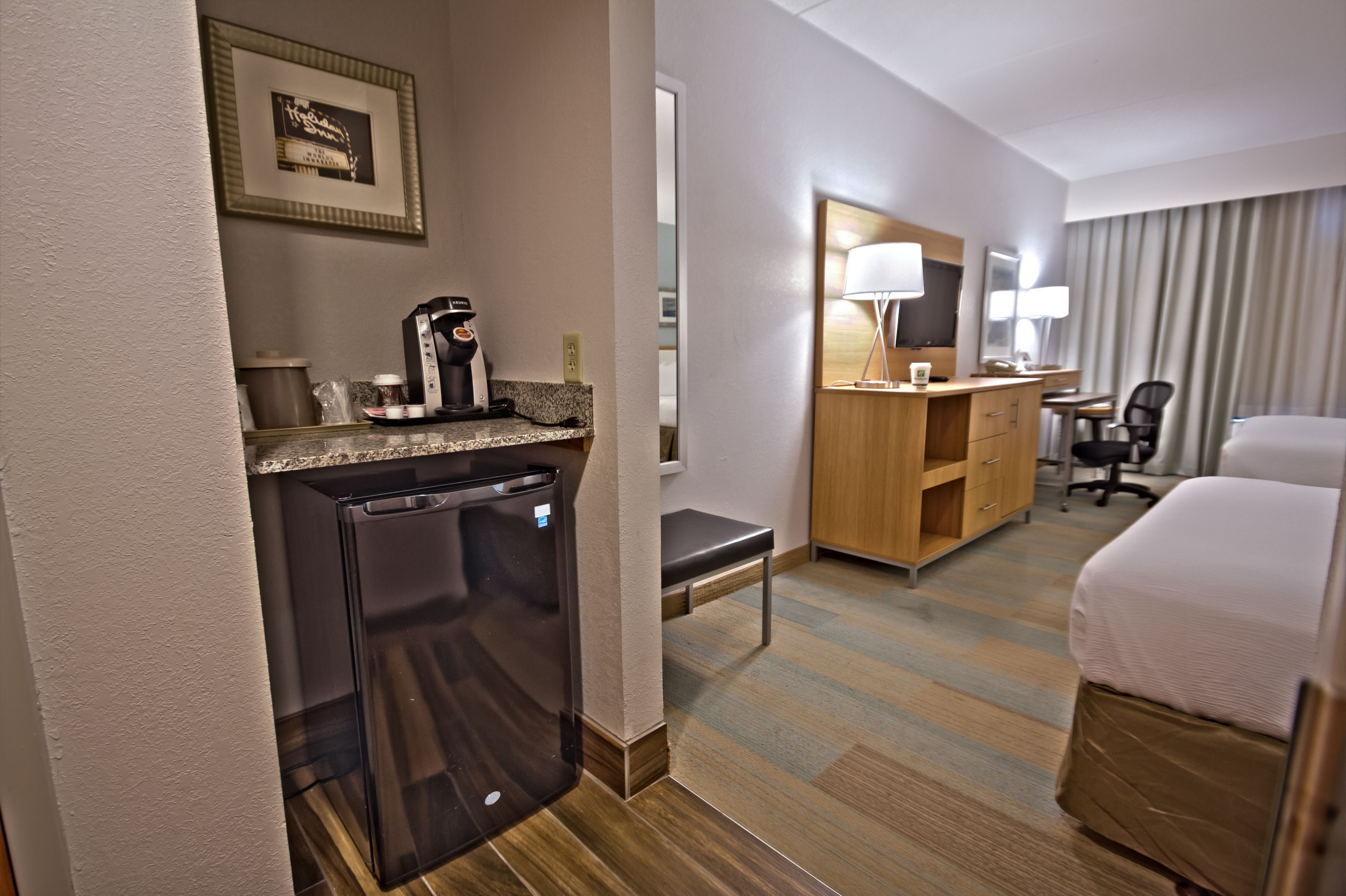 Une chambre d’hôtel comprenant un lit, un bureau avec une chaise, un réfrigérateur, une machine à café et une lampe.
