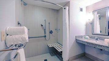 Baño con ducha, barras de apoyo, lavabo y espejo.
