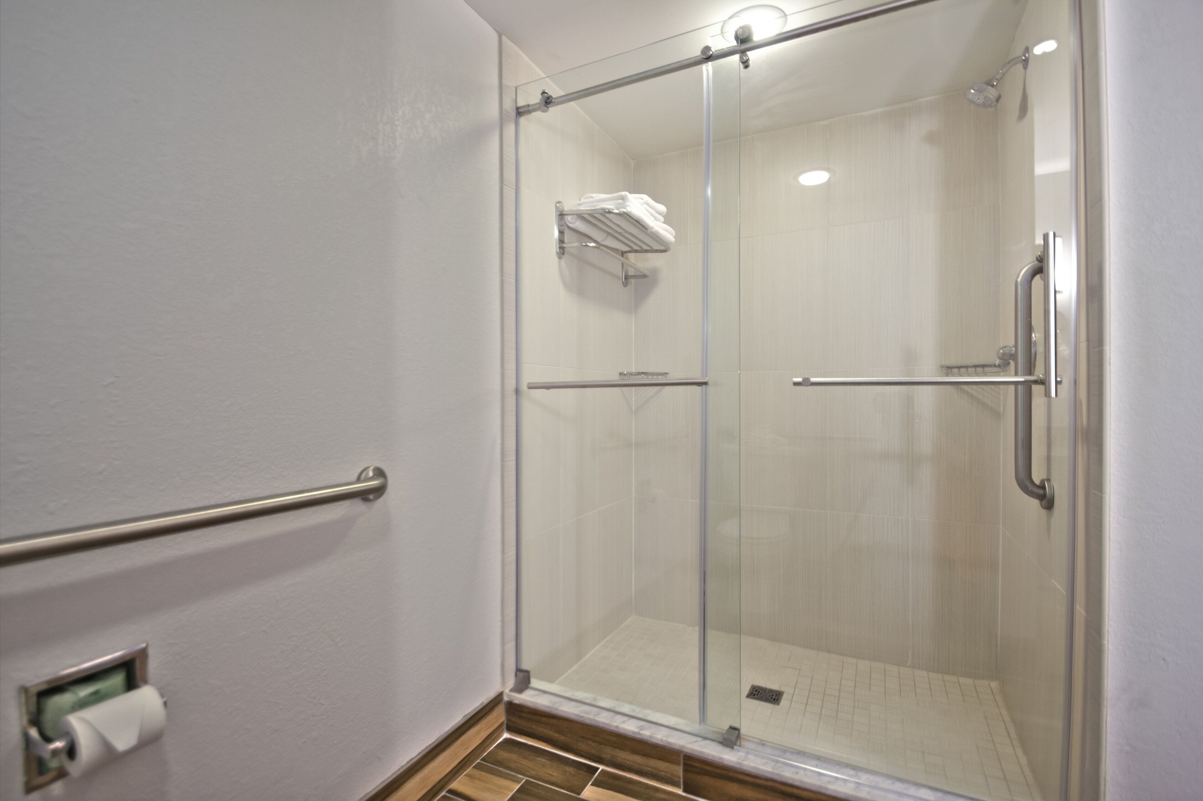 A glass-enclosed shower with a handrail, a towel rack, and a toilet paper holder.