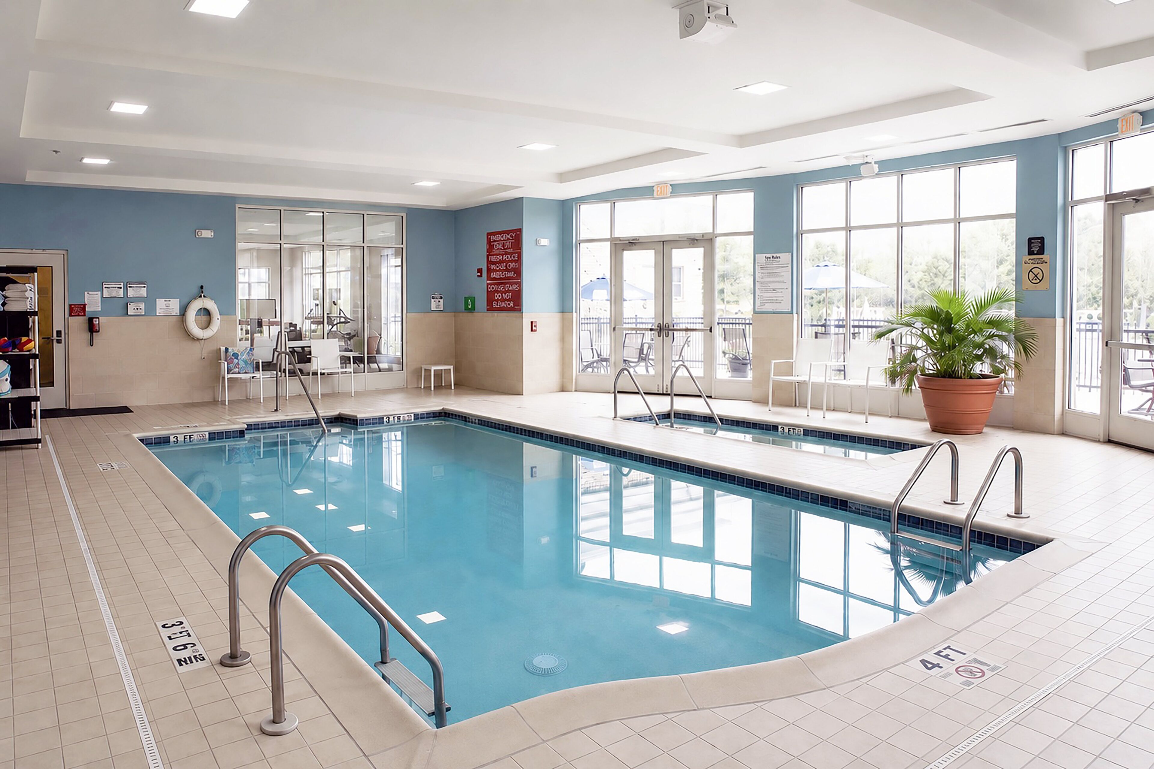 En indendørs swimmingpool med tydelige markeringer, en redningsbås og en potteplante.