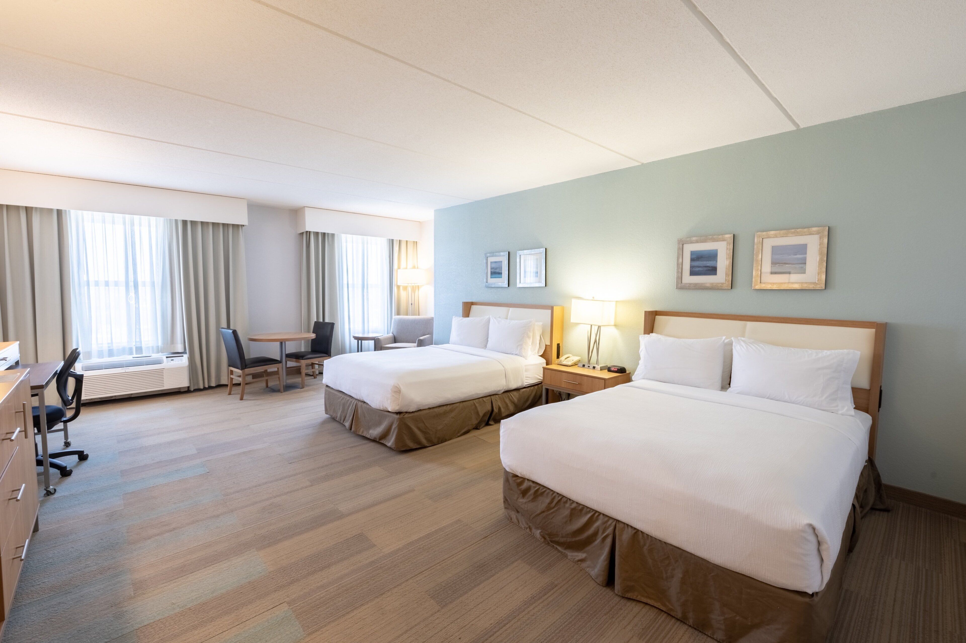 A hotel room with two beds, a desk, a chair, a lamp, and a window with curtains.