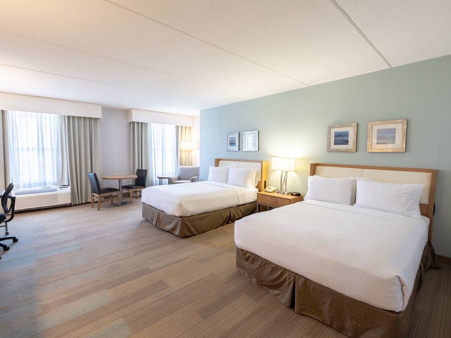 A hotel room with two beds, a desk, a chair, a lamp, and a window with curtains.