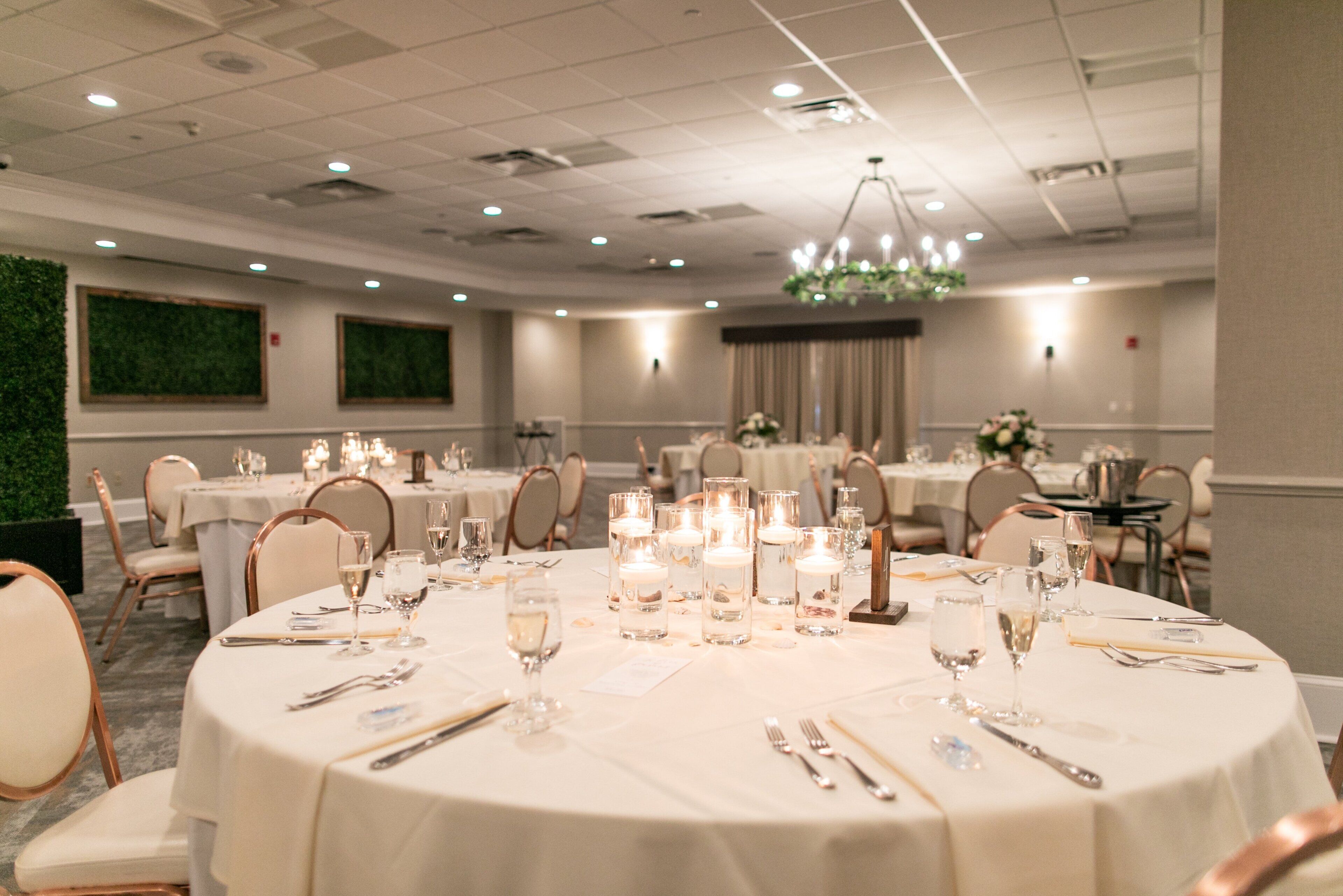 A banquet hall with round tables set for a formal event, featuring candles, glassware, and floral centerpieces.