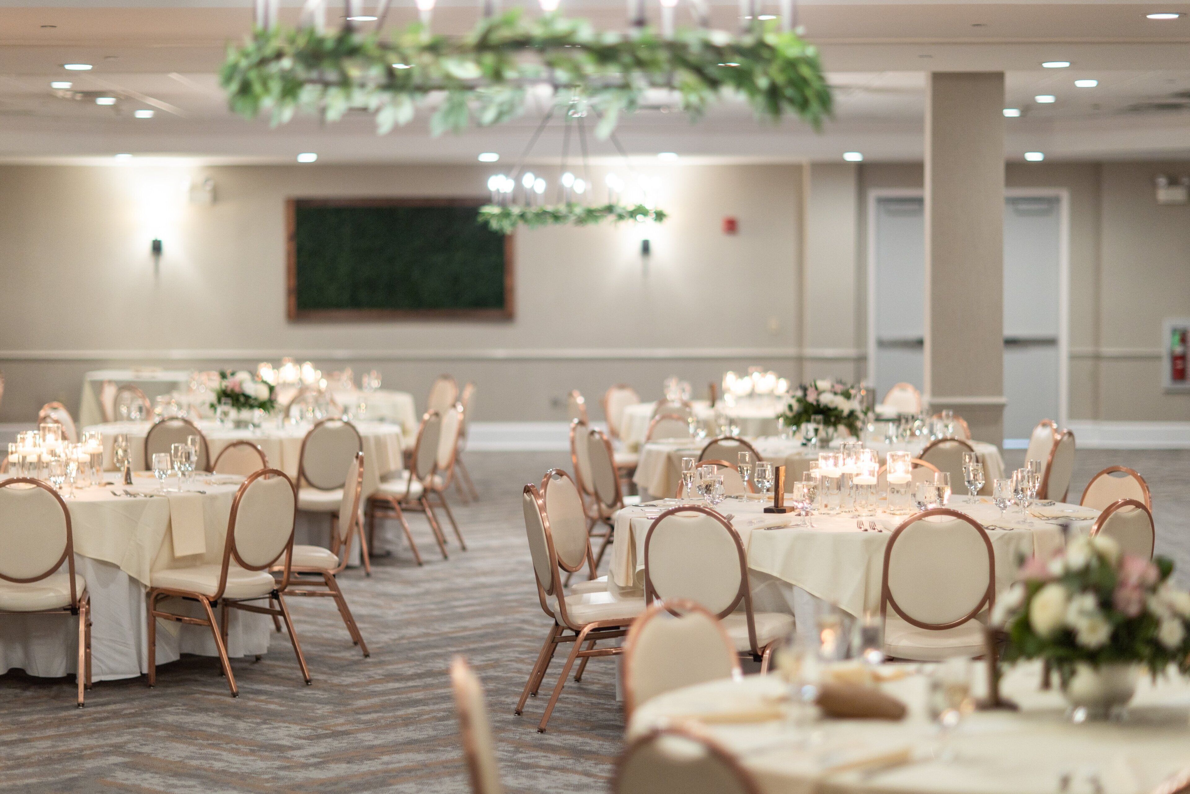 A banquet hall with round tables set for a formal event, featuring white tablecloths, chairs, and floral centerpieces.