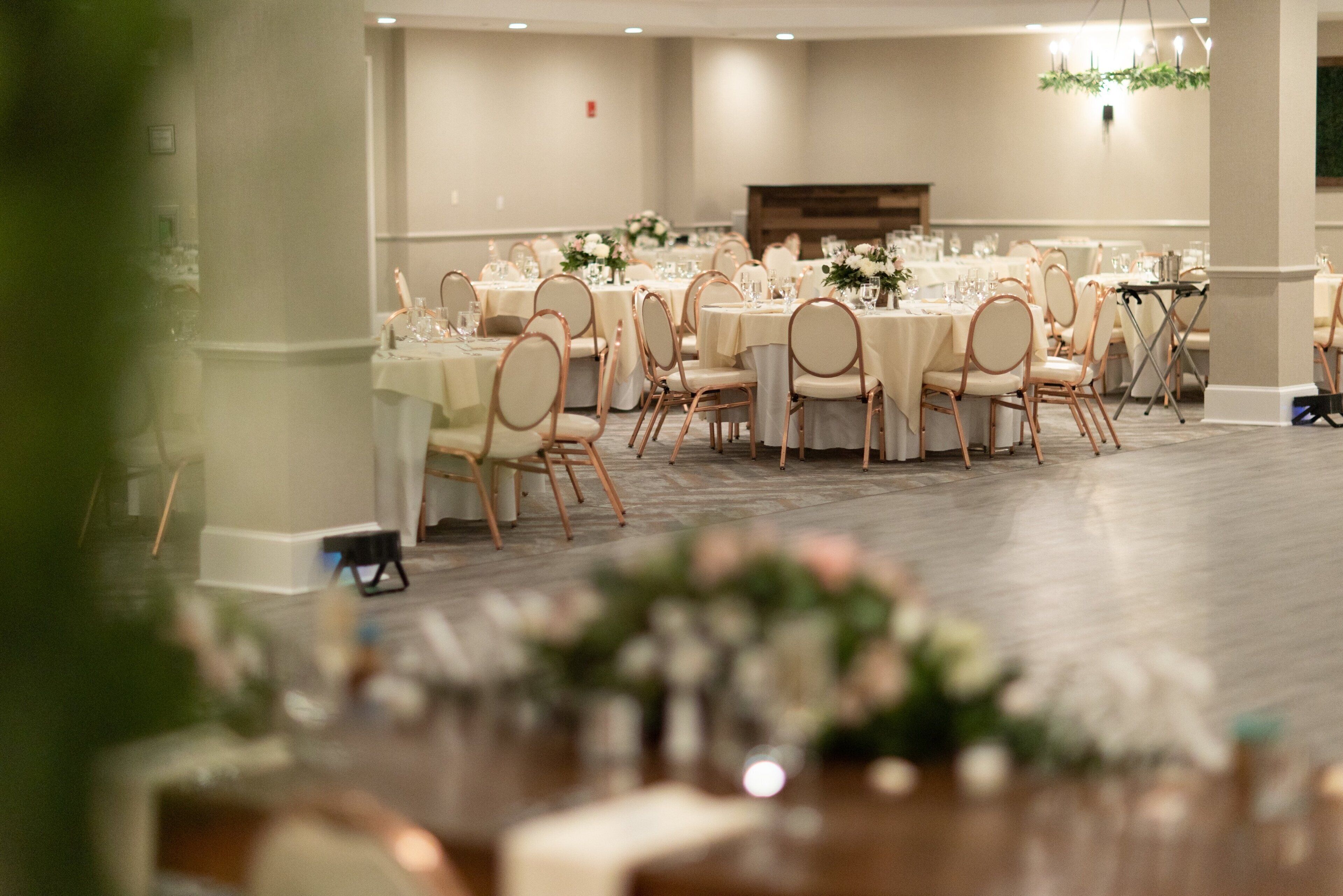 Un salón de banquetes con mesas redondas, sillas y centros de mesa florales.