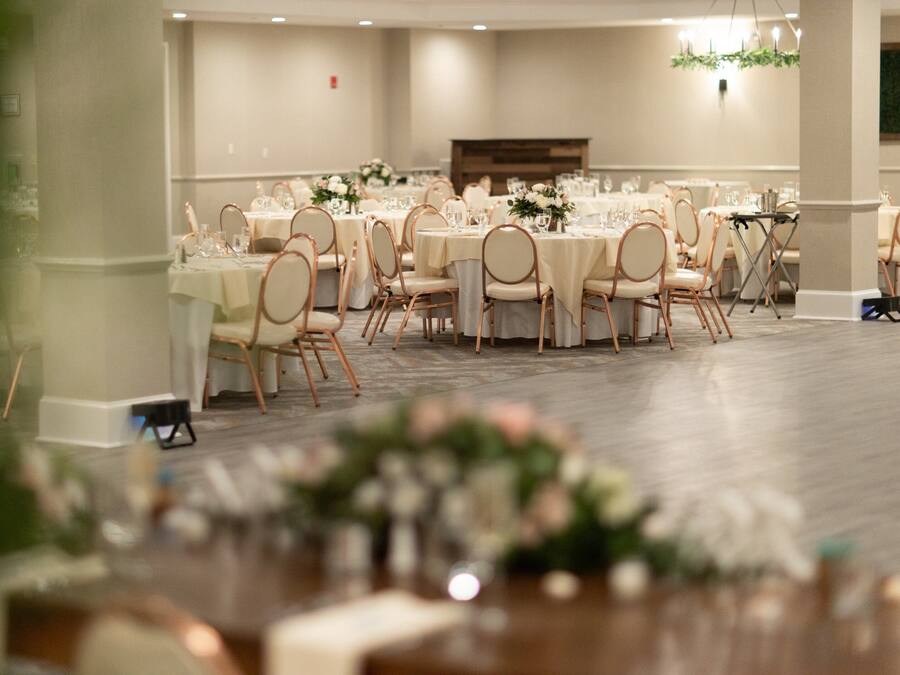 Un salón de banquetes con mesas redondas, sillas y centros de mesa florales.