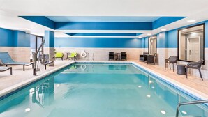 An indoor swimming pool with blue and white walls, a sunken seating area, and a door leading to another room. - Hampton Inn & Suites Lathrop (Lathrop)