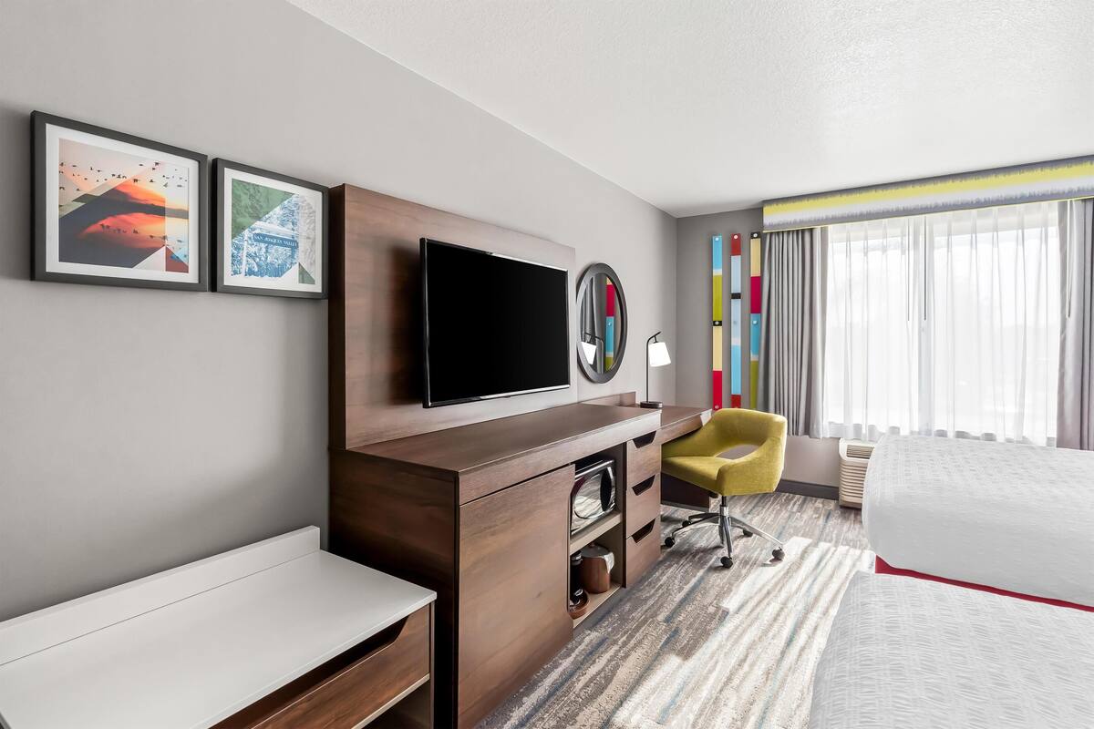 A hotel room with a bed, a desk, a chair, a TV, and two framed pictures on the wall.
