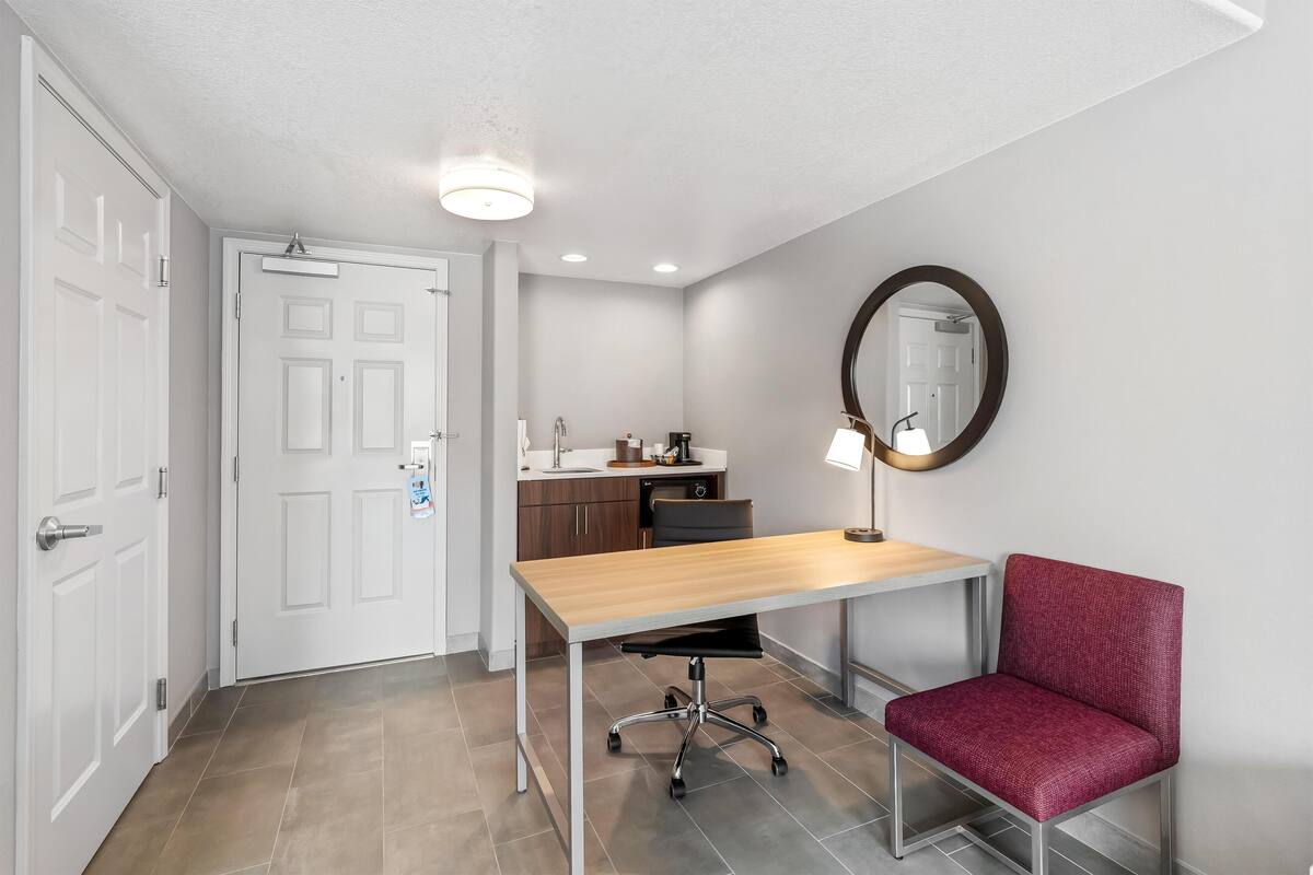 A room with a wooden desk, a red chair, a mirror, and a door.