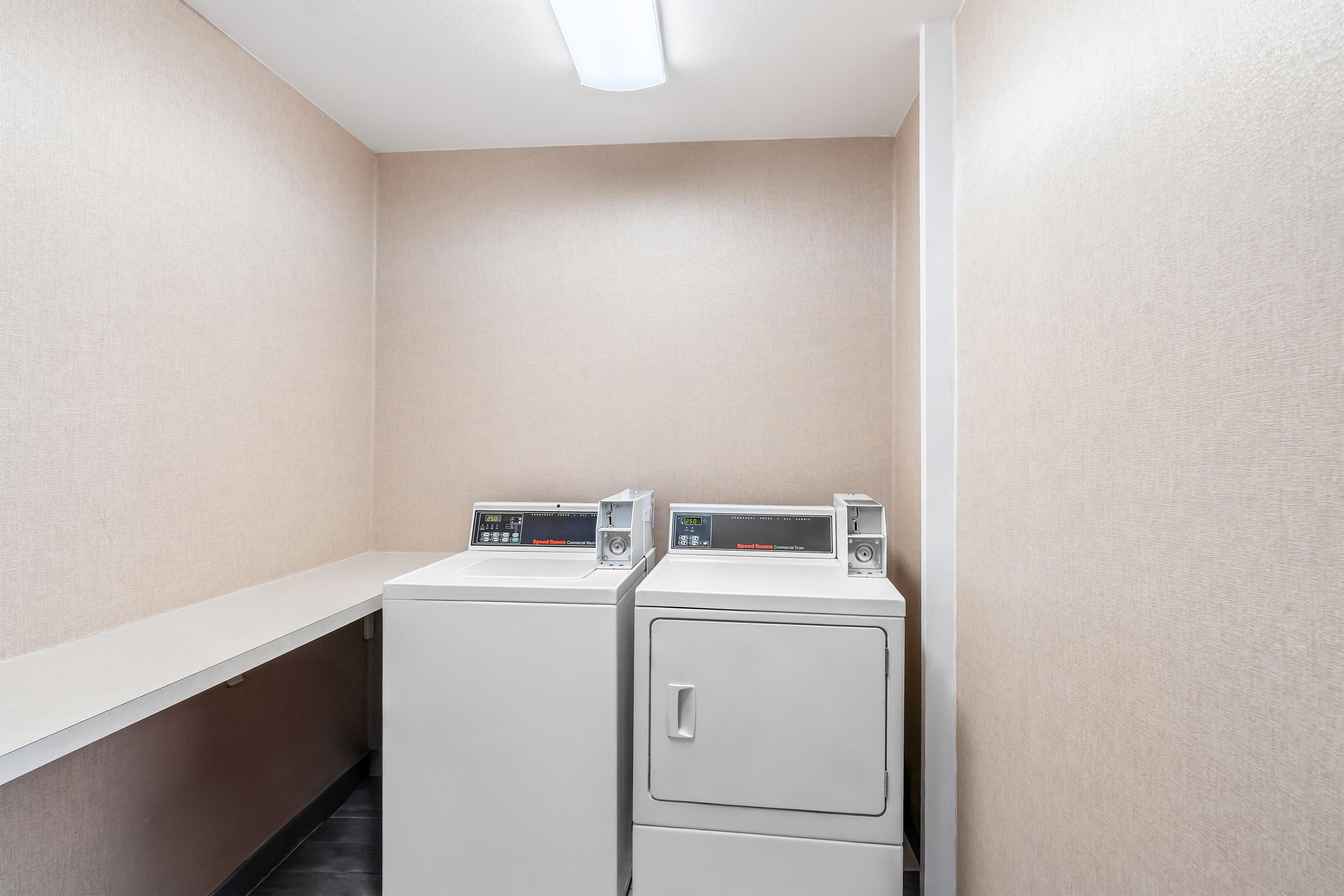 A laundry area with two washing machines and a dryer, a white countertop, and a wall-mounted control panel.