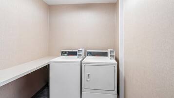 A laundry area with two washing machines and a dryer, a white countertop, and a wall-mounted control panel.