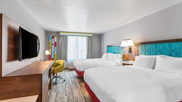 Habitación de hotel con dos camas, un escritorio, un televisor, una silla y una ventana con cortinas.