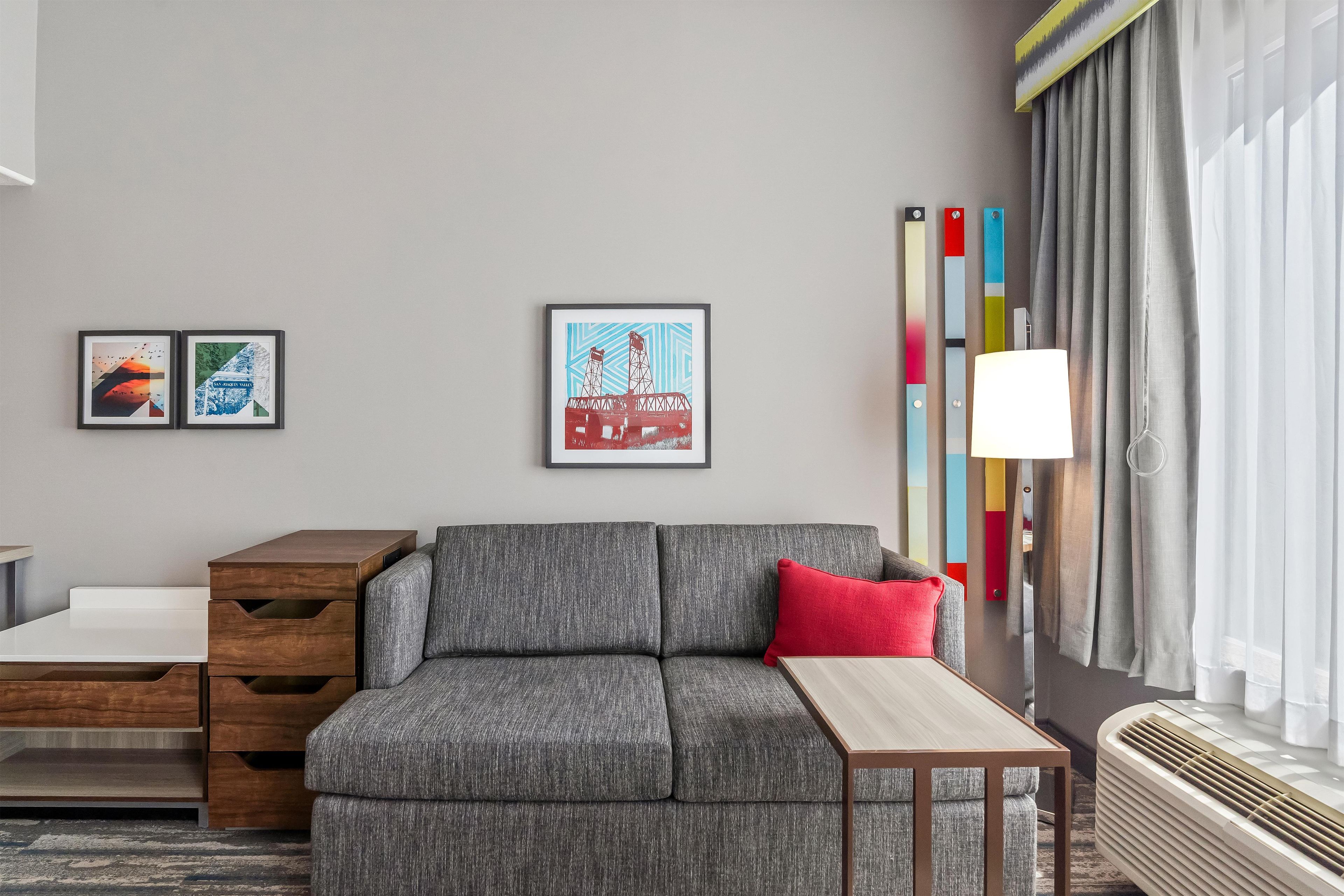 A modern living room with a grey sofa, a wooden side table, a small table, and a colorful abstract painting on the wall.