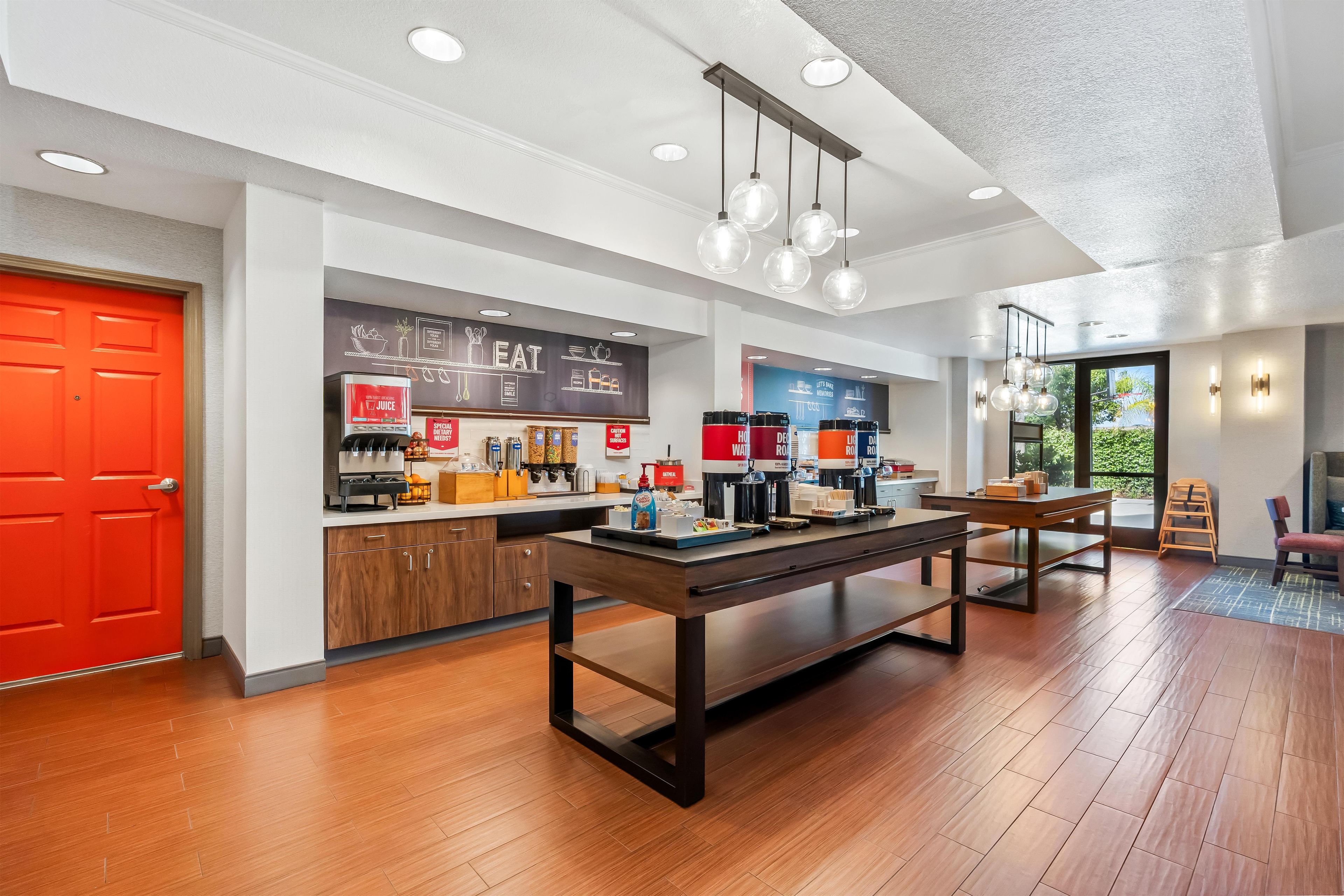 Un café moderno con una mesa y sillas de madera, una puerta roja y un menú en pizarra.