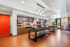 Un café moderno con una mesa y sillas de madera, una puerta roja y un menú en pizarra.