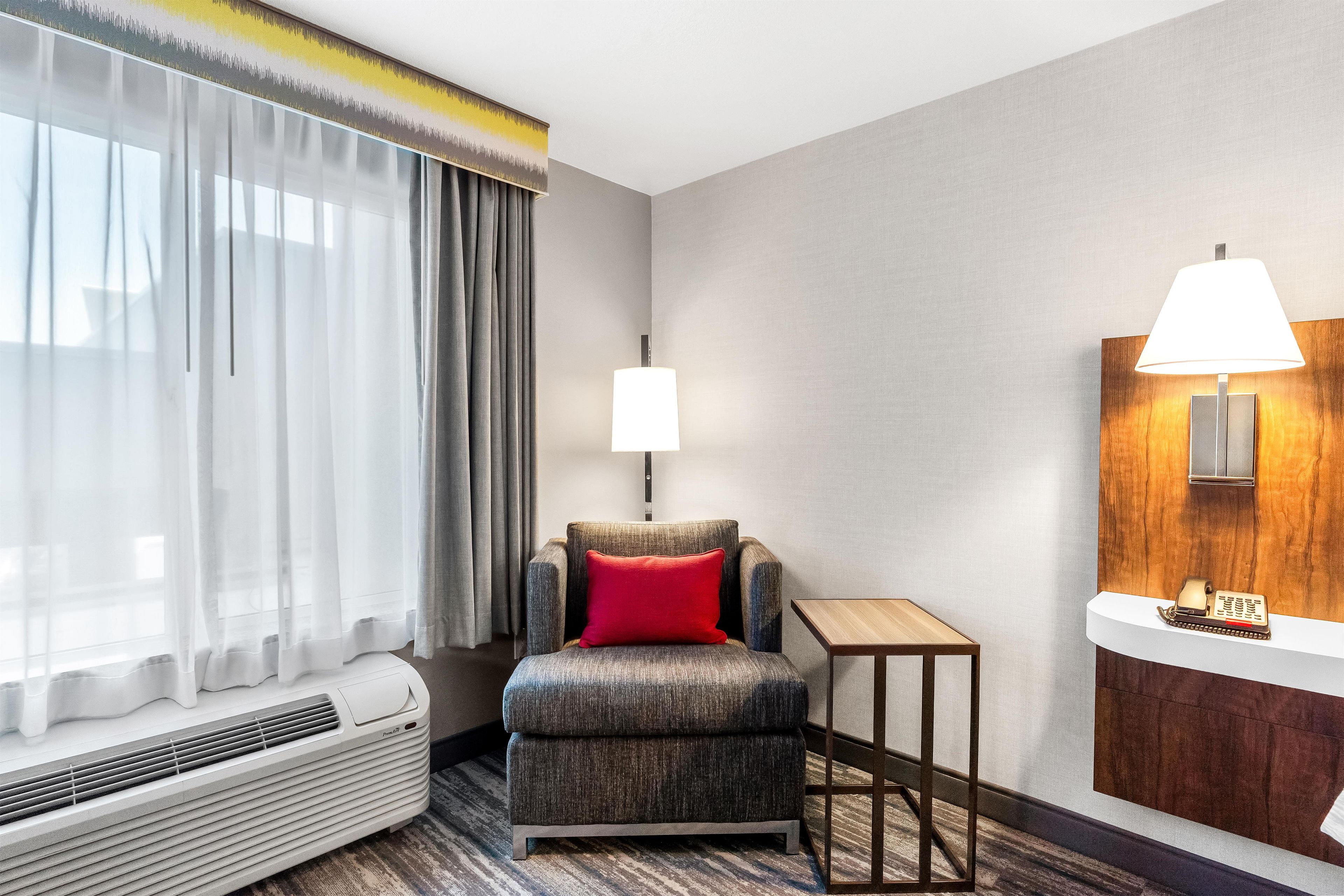 Habitación de hotel con sofá, una mesita, lámpara y ventana con cortinas.