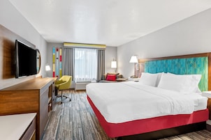 A hotel room with a bed, a desk, a TV, a chair, a lamp, and a window with curtains.
