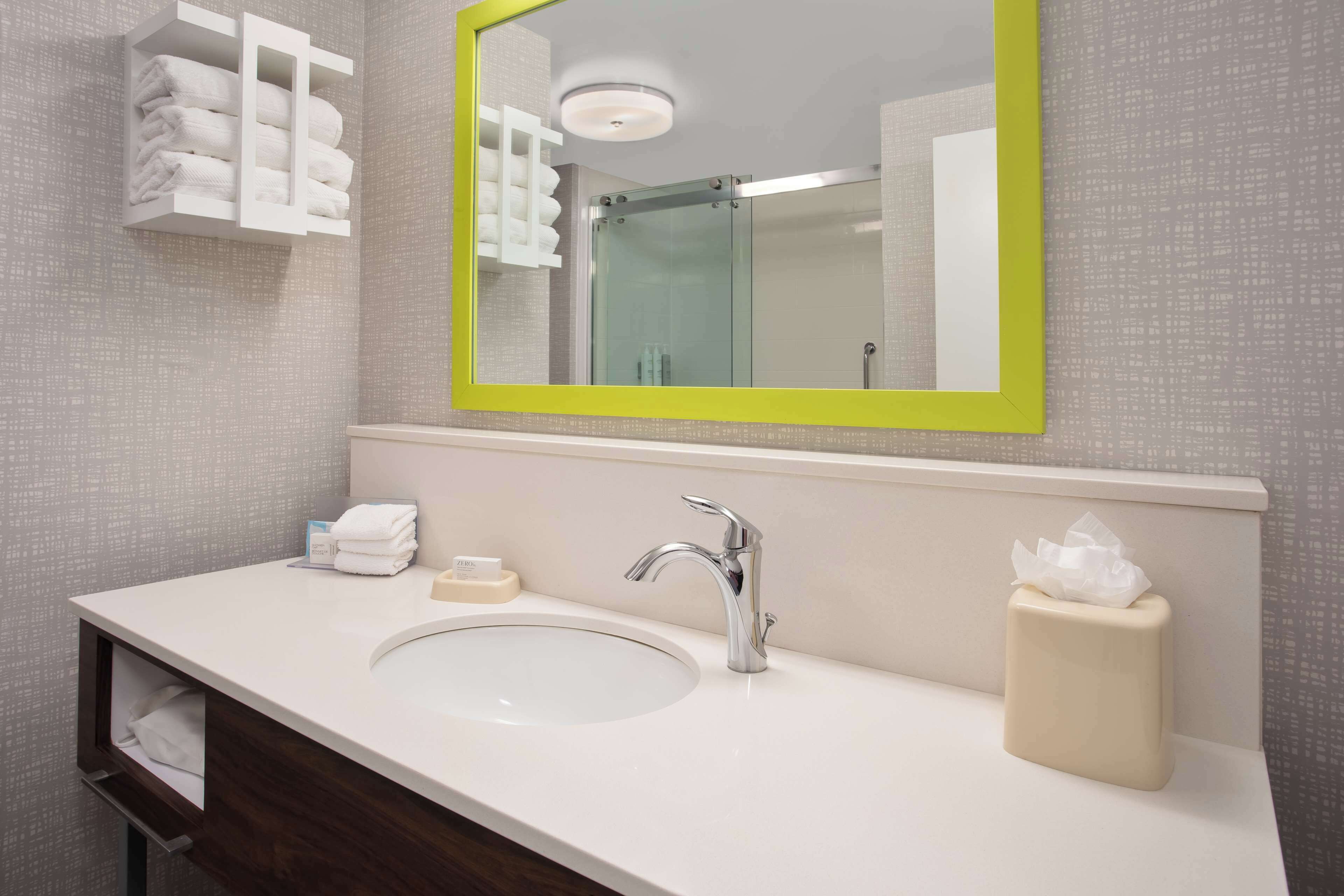 A bathroom with a white sink, a mirror with a yellow frame, a towel rack, and a glass shower enclosure.