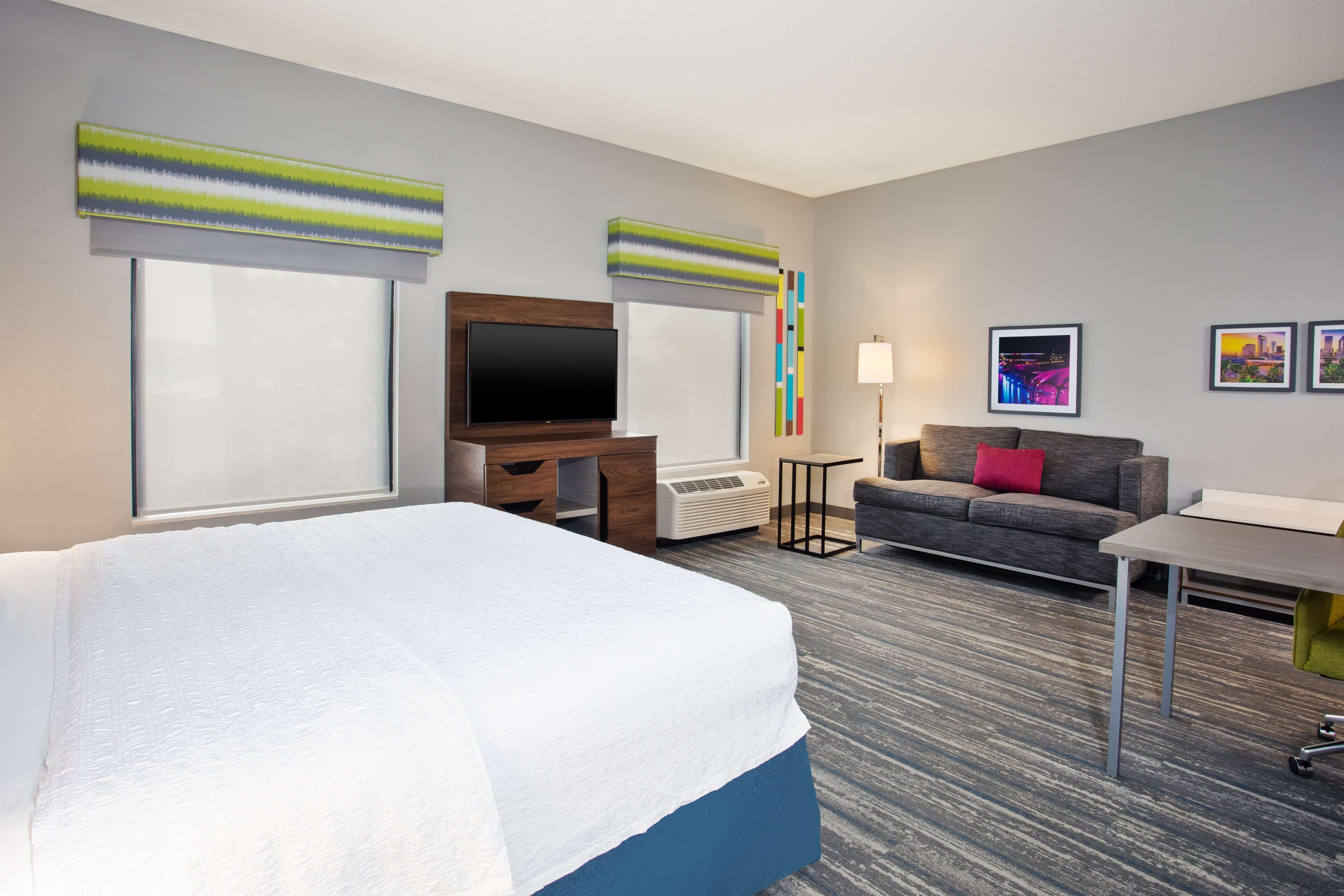 Una habitación de hotel con cama, sofá, televisión, escritorio y lámpara.