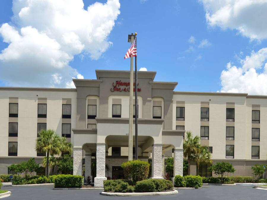 Un hotel Hampton Inn Suites con entrada central, enseña y jardines bien cuidados.