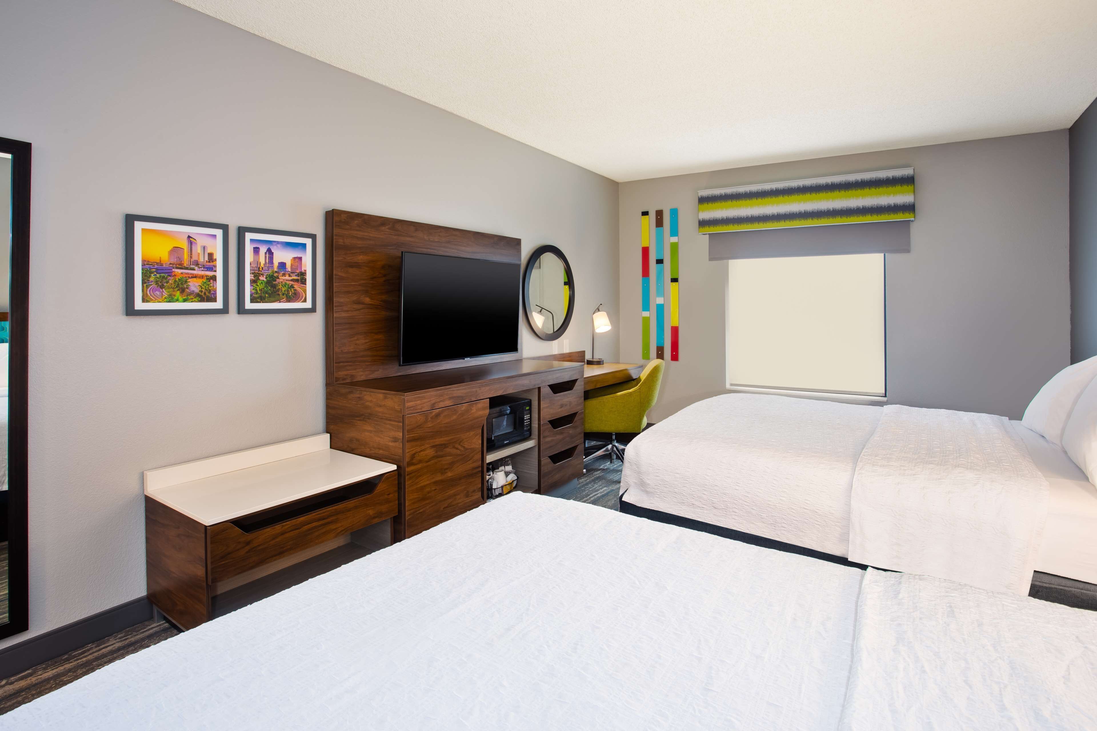 Quarto de hotel com duas camas, uma escrivaninha, televisão de tela plana, espelho e janela com vista.