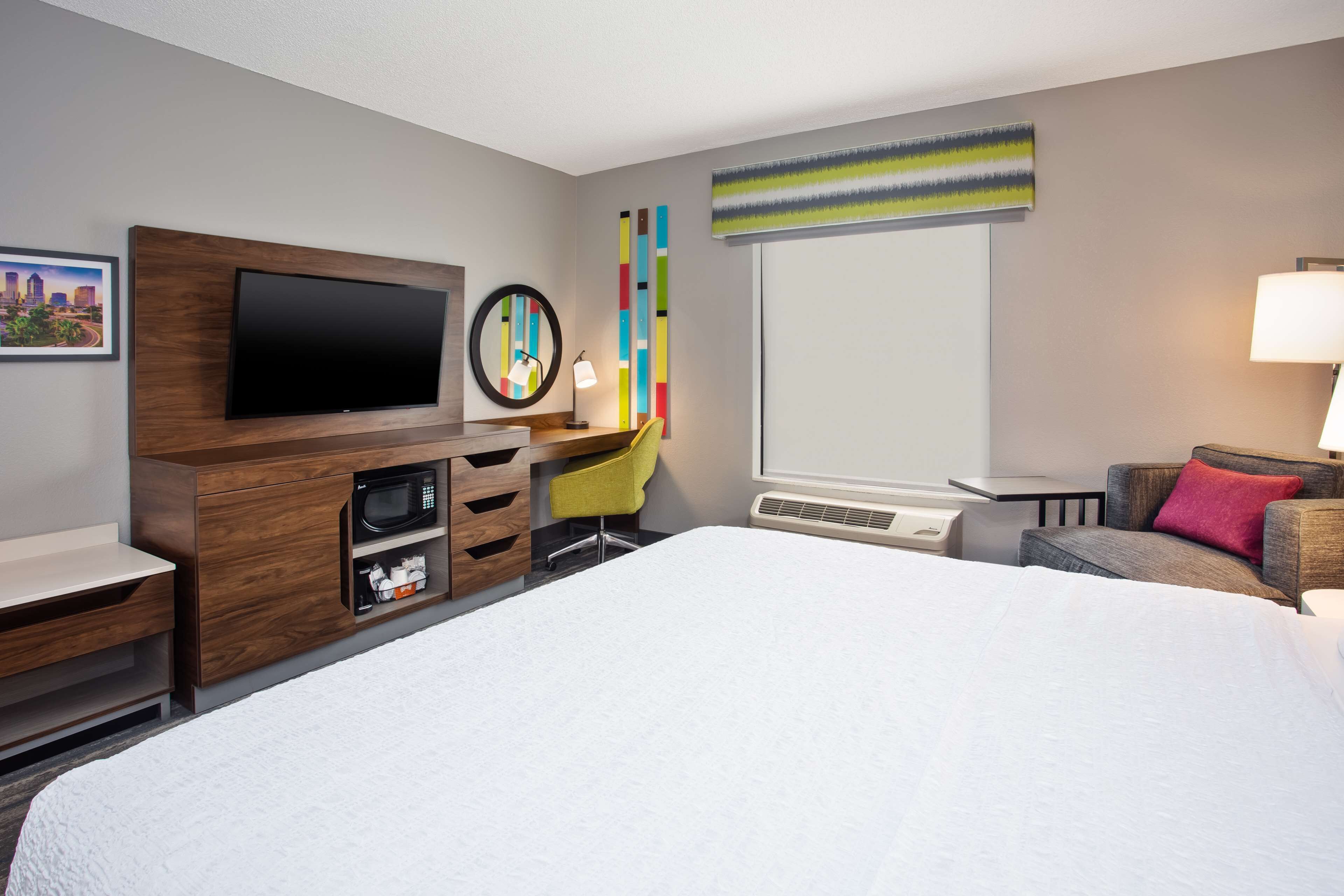 Habitación de hotel con una cama grande, un televisor de pantalla plana, microondas, escritorio pequeño, silla y sofá con almohada.