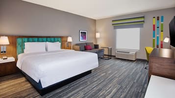 A hotel room with a large bed, a desk, a chair, a TV, and a window.