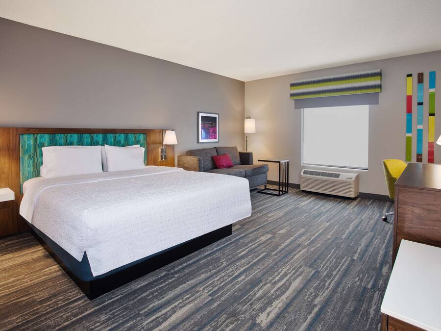 A hotel room with a large bed, a desk, a chair, a TV, and a window.